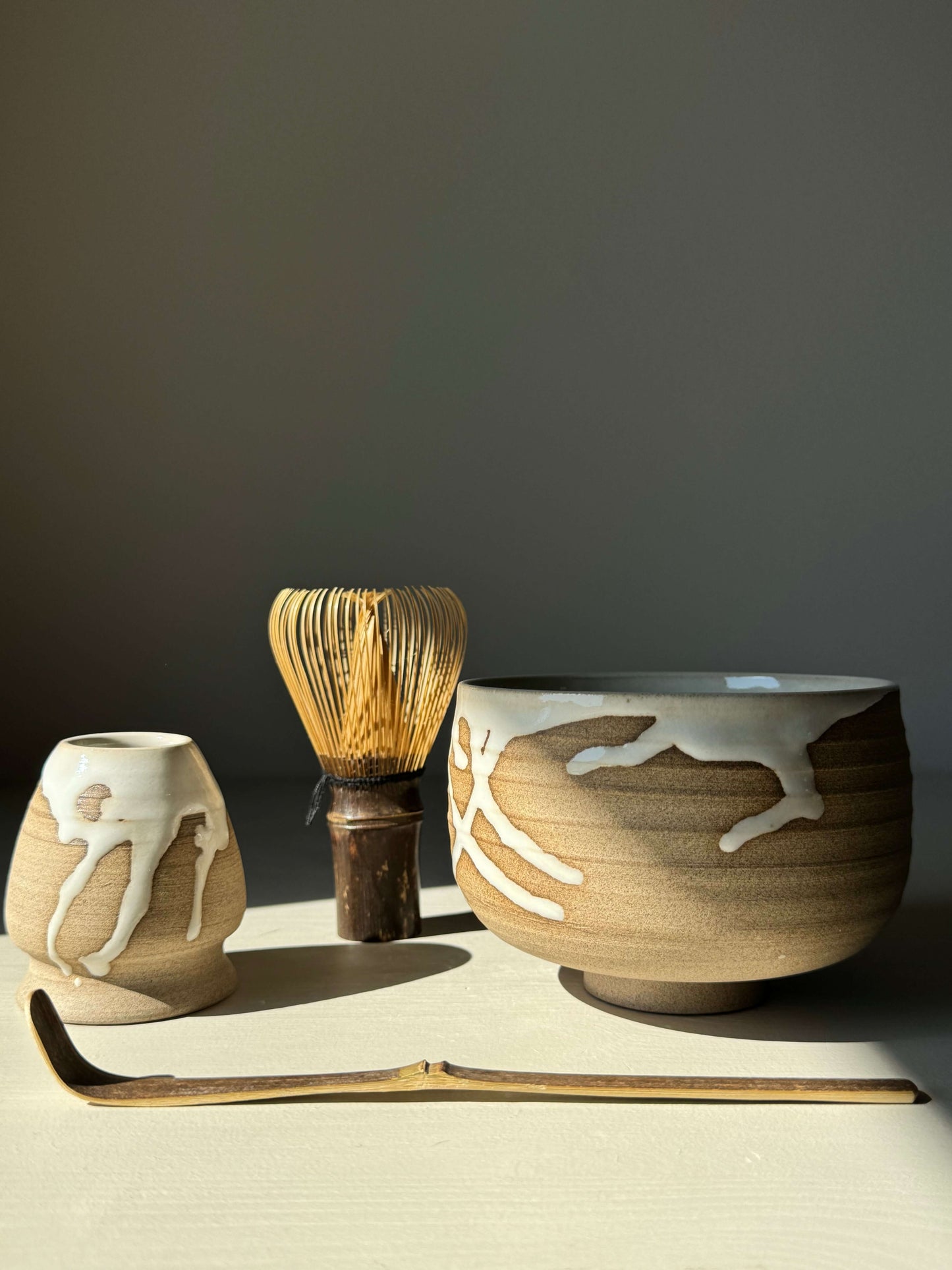Handmade Yuki Series #06 Matcha Bowl with toffee clay and white glaze, accompanied by a whisk and scoop on a neutral background.