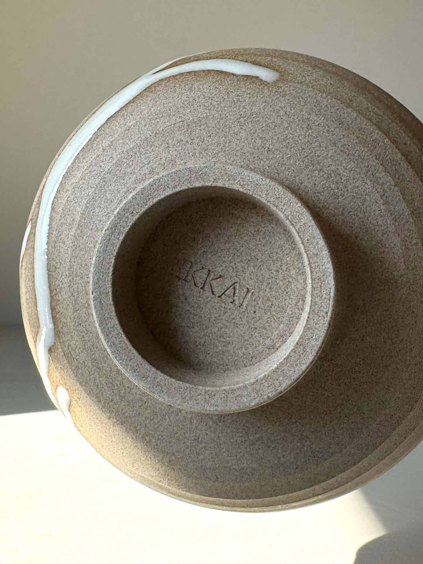Underside view of handmade Matcha Bowl from Yuki Series #01, featuring toffee clay and glossy white glaze in natural light.
