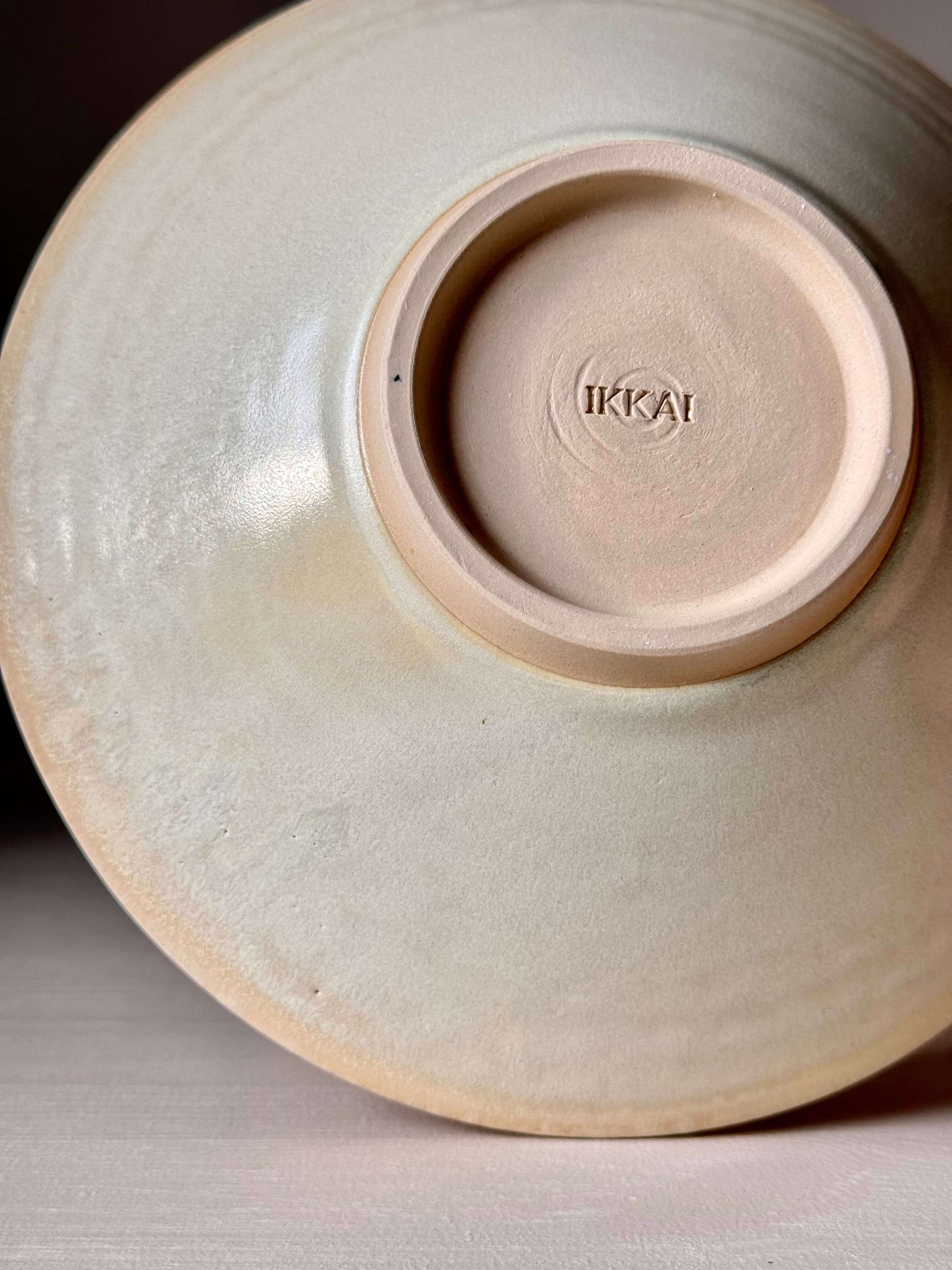 Underside view of a handmade Moonstone glaze stoneware dish, featuring wheel-thrown texture and artisan maker's mark.