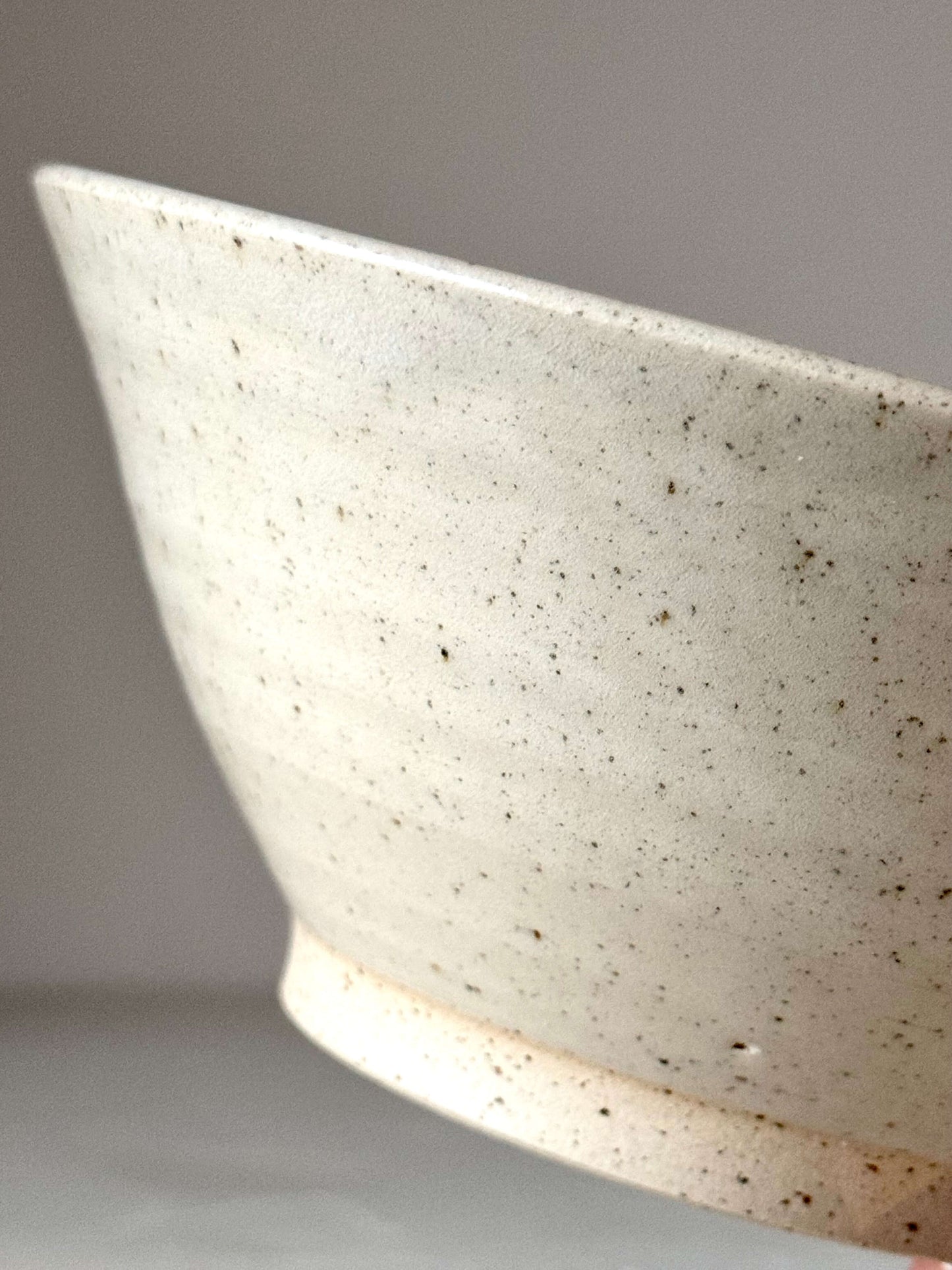 Close-up of a speckled stoneware ceramic bowl with a cream glaze, showcasing handmade texture and detailing.