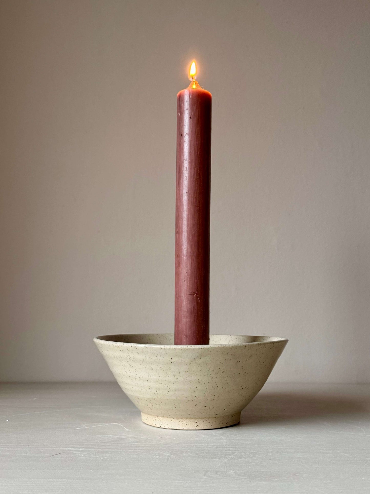 Handmade clear glaze candlestick holder with lit candle, featuring a rustic stoneware design and iron oxide spots, 7cm tall, 17.5cm wide.