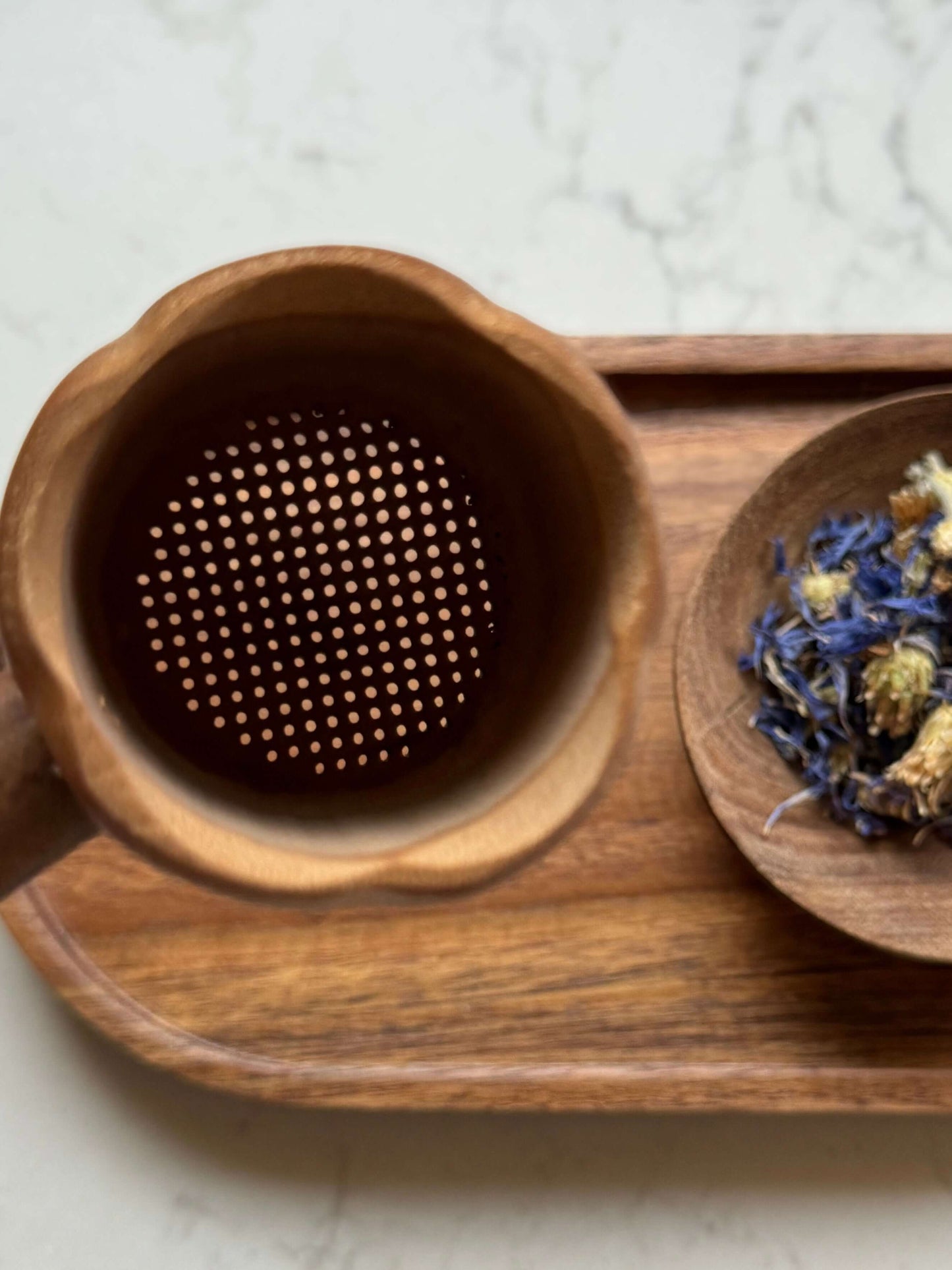Handmade bamboo tea strainer with root handle alongside dried flowers on wooden tray, ideal for rustic tea rituals.