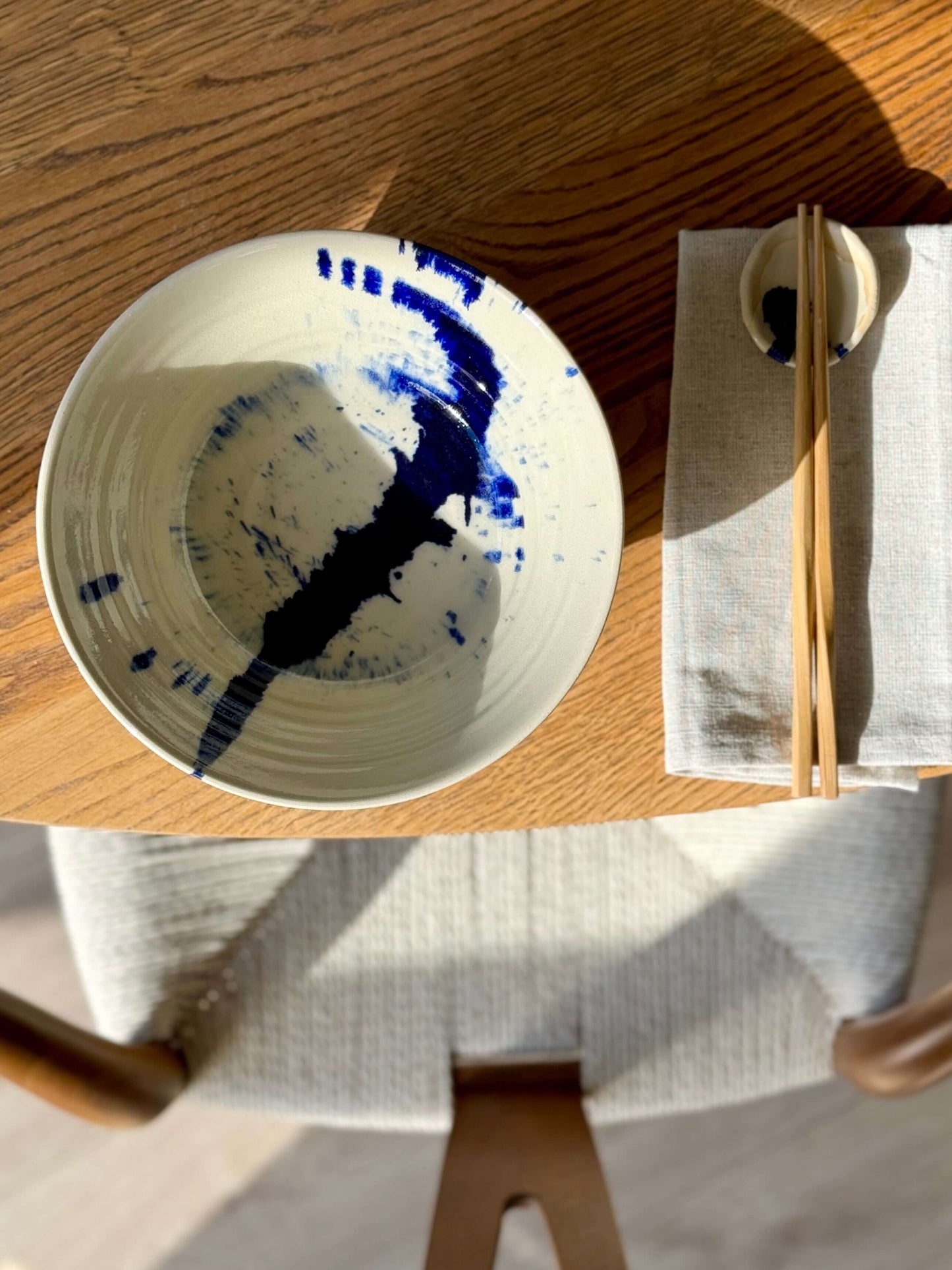 Handmade ceramic breakfast bowl from the Gosu Series with cobalt blue accents, placed on a wooden table with chopsticks and napkin.