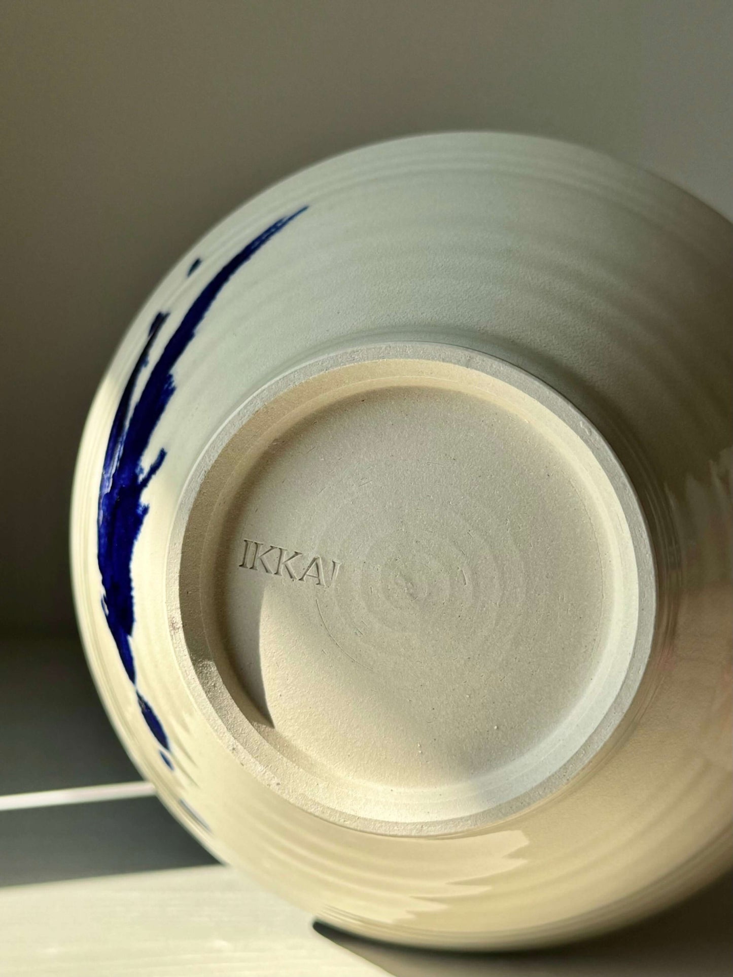 Bottom of handmade Gosu Series ceramic bowl with cobalt blue accents and "IKKAI" marking, showcasing craftsmanship detail.