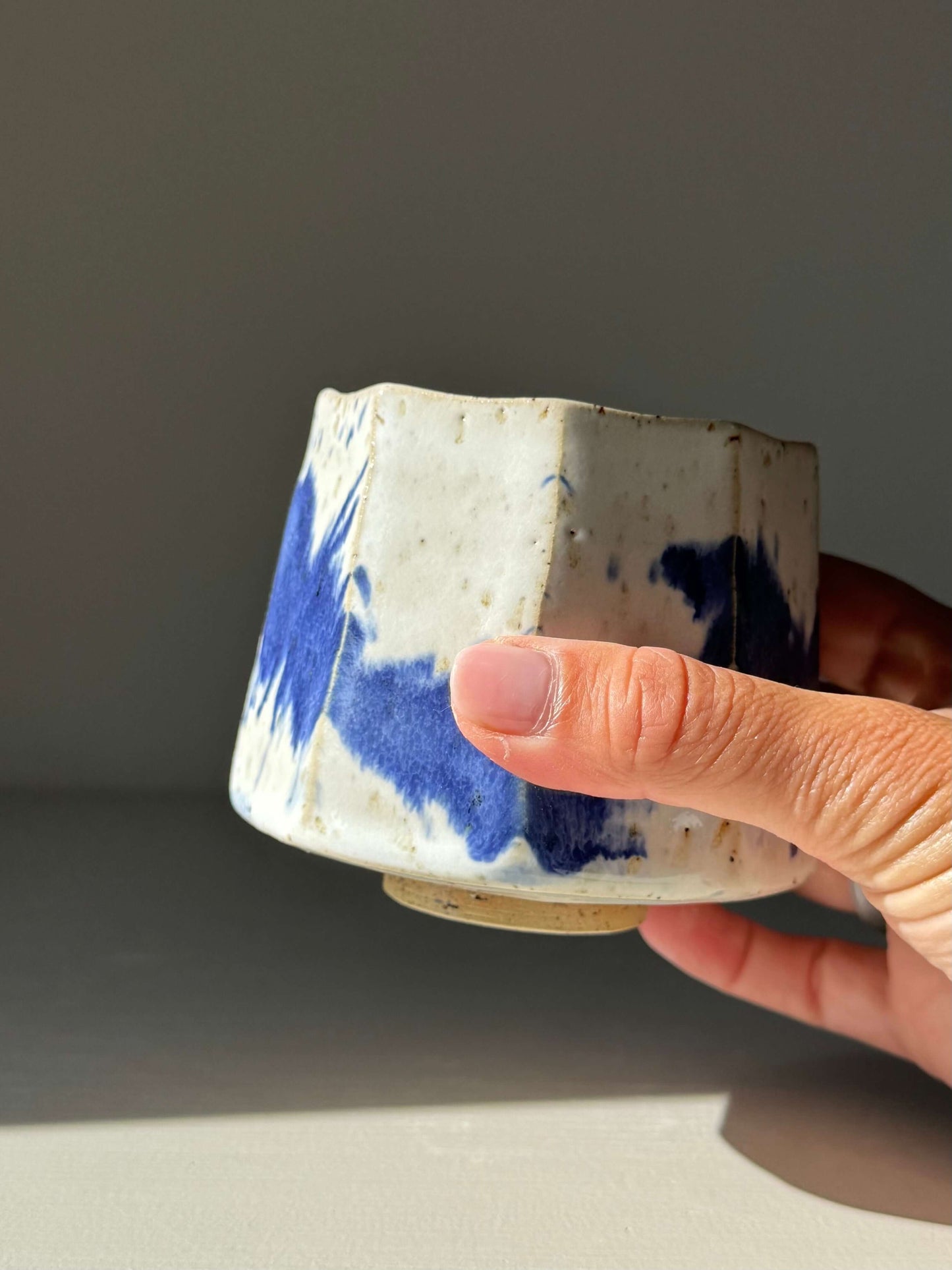 Faceted Cup – Cobalt Blue & Glossy White #04, handmade ceramic with hand-carved angles and cobalt blue splashes, held in hand.