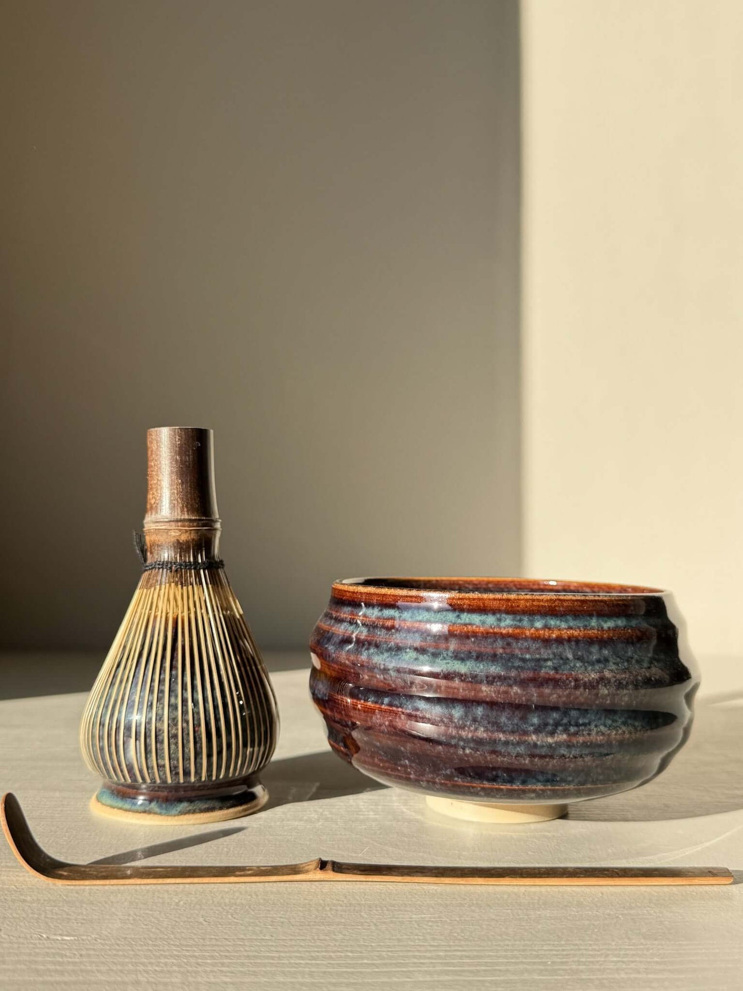 Matcha Bowl - Glossy Blue #02 with chasen and chashaku in soft lighting, highlighting the bowl's unique flowing blue design and raised foot.