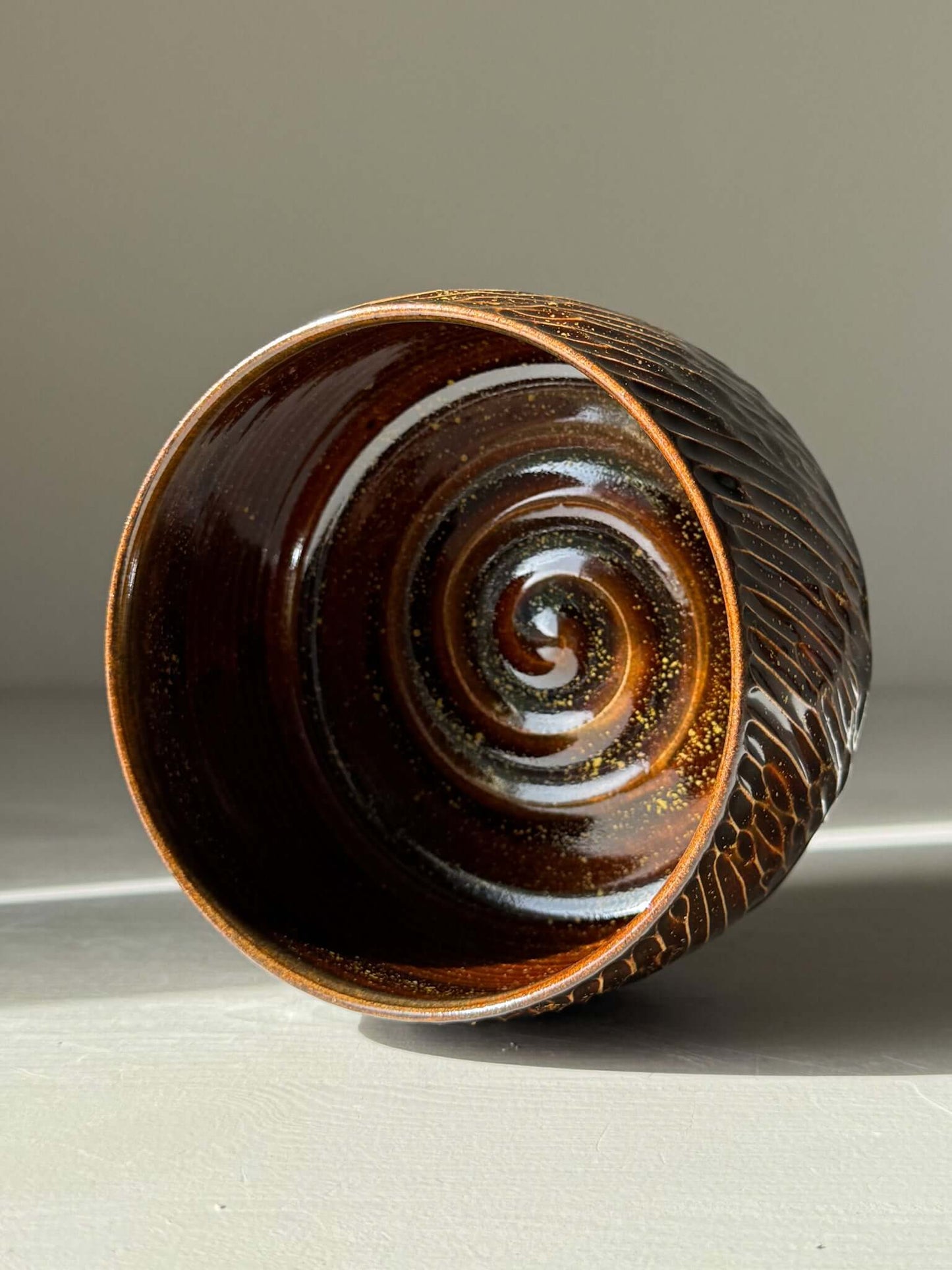 Matcha Bowl – Kinsei #05, handmade ceramic with a spiral of gold and orange glaze, showcasing a rich, glossy brown carved exterior.