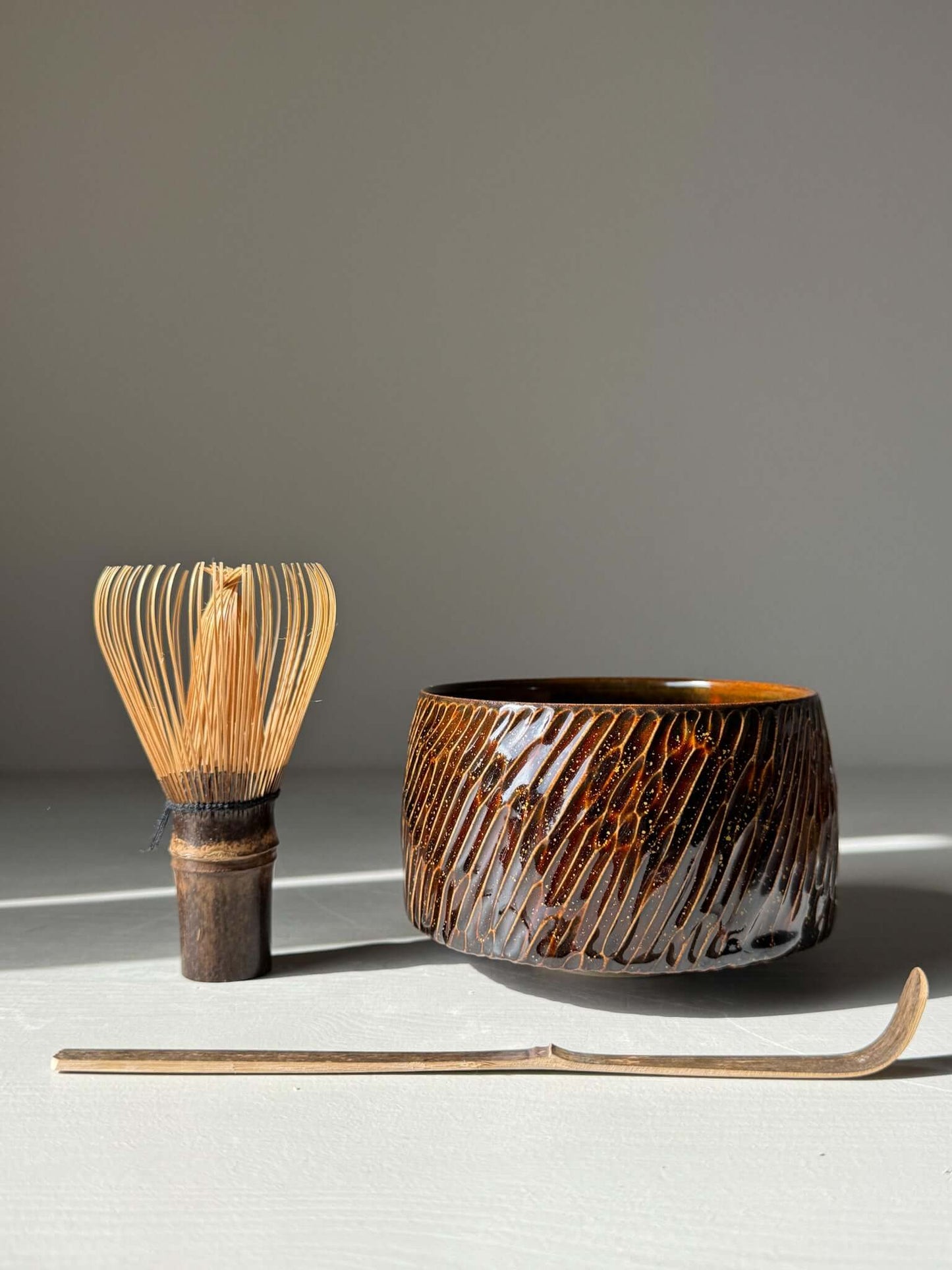 Handmade ceramic Matcha Bowl – Kinsei #05 with carved glossy brown exterior, spiral gold interior, and matcha whisk on display.