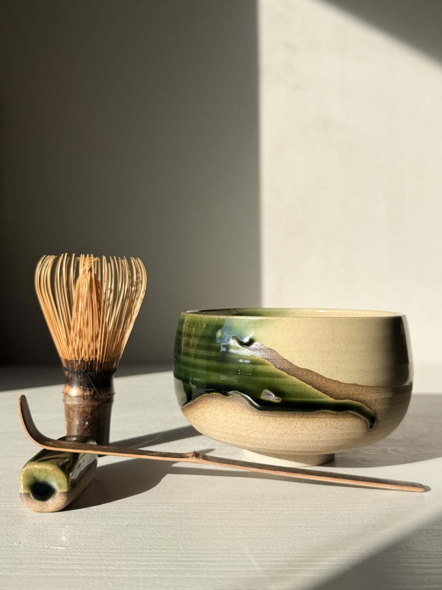 Handmade ceramic Matcha Bowl – Mori #02 with green and brown glazes, accompanied by traditional matcha whisk and scoop.