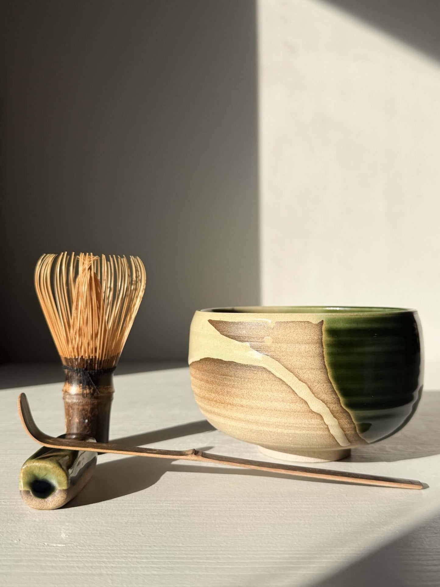Matcha Bowl – Mori #03 with handmade ceramic whisk set, featuring natural stoneware and layered green-brown glazes on a sunny table.