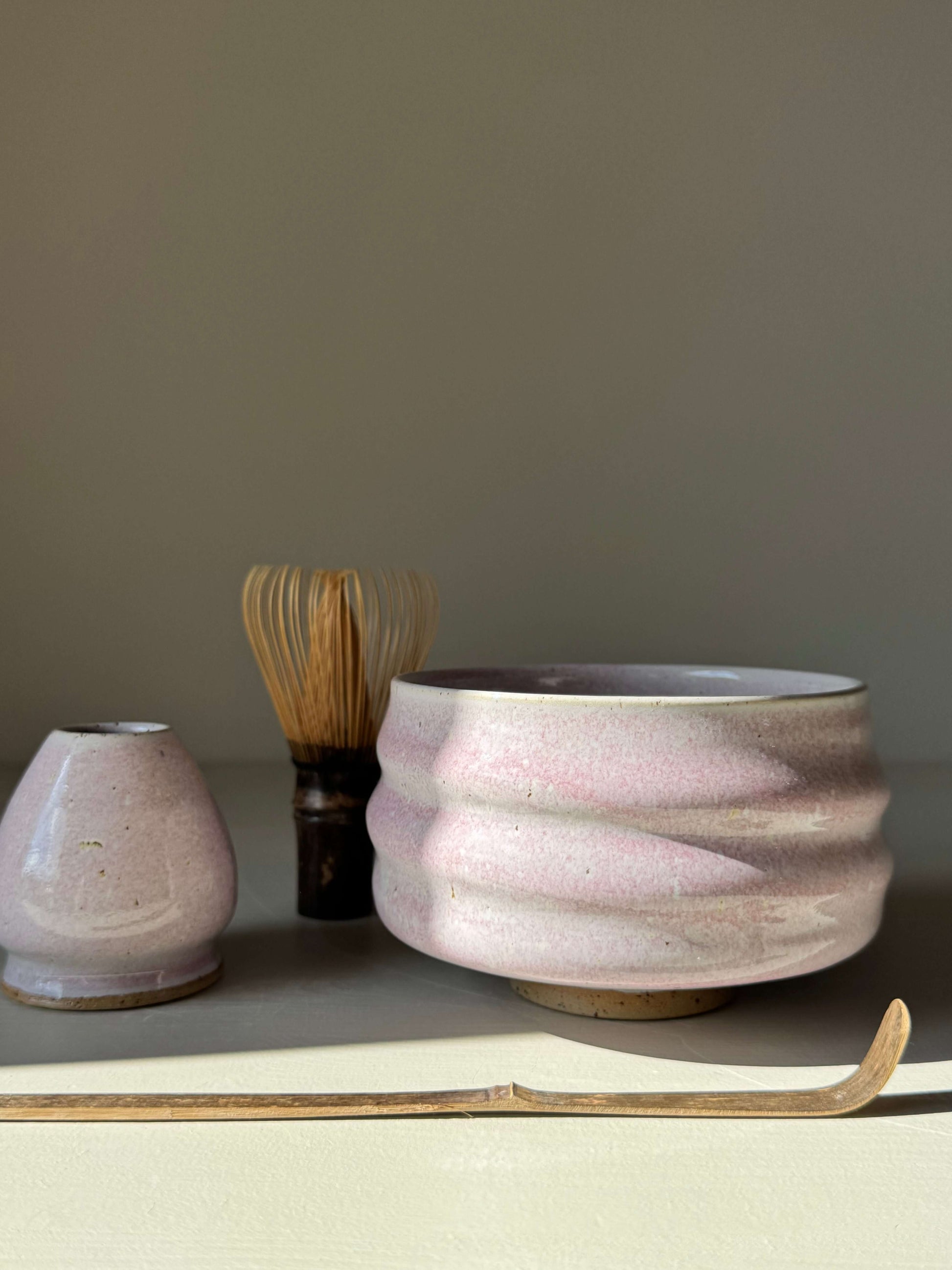 Handmade ceramic Matcha Bowl - Pale Pink with dreamy glaze, sculpted ridges, and delicate charm next to a whisk and utensil.
