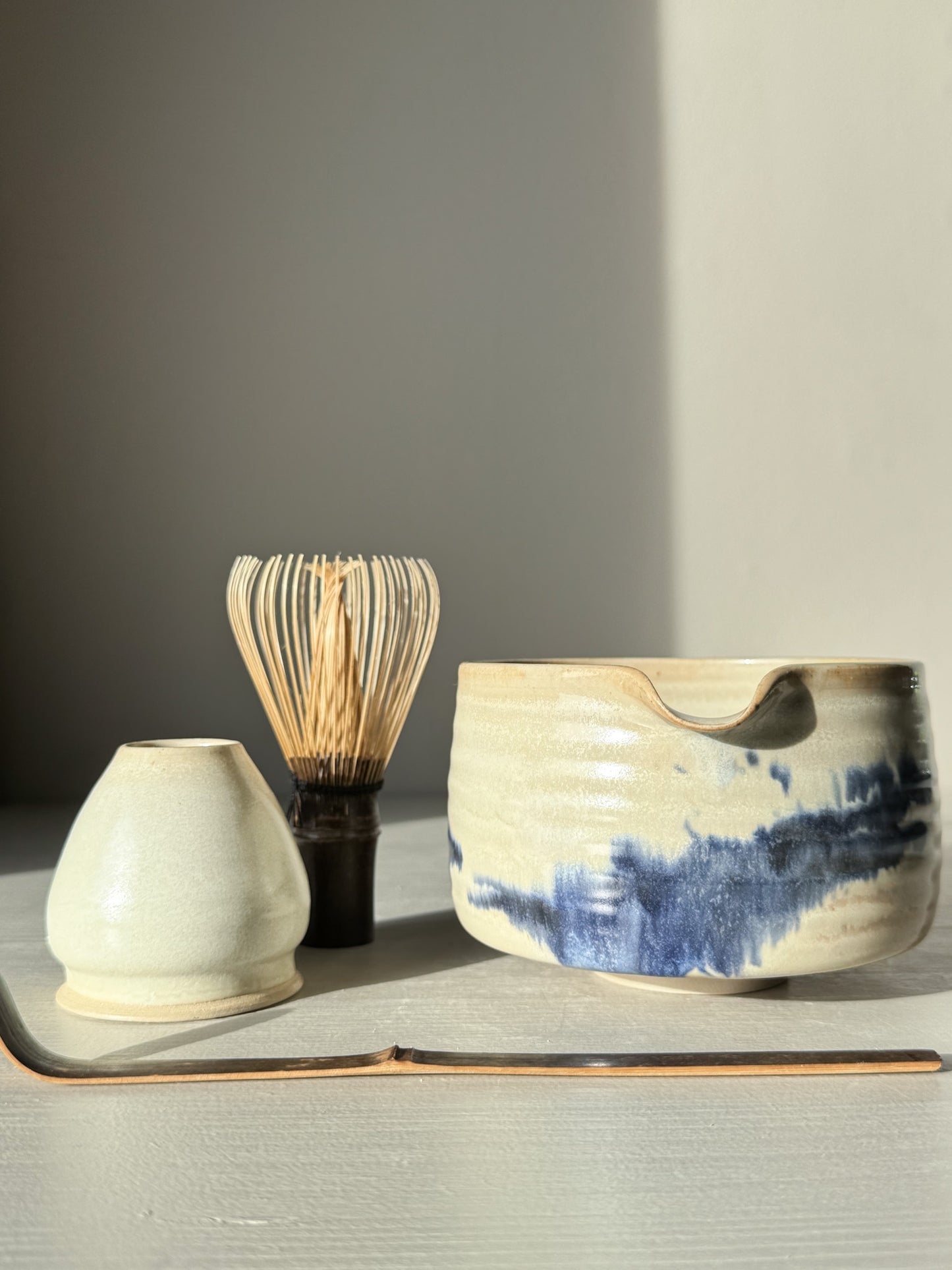 Matcha bowl Spout - Moonstone & Blue #03 with hand-splashed cobalt glaze beside matcha whisk and scoop on a tabletop.