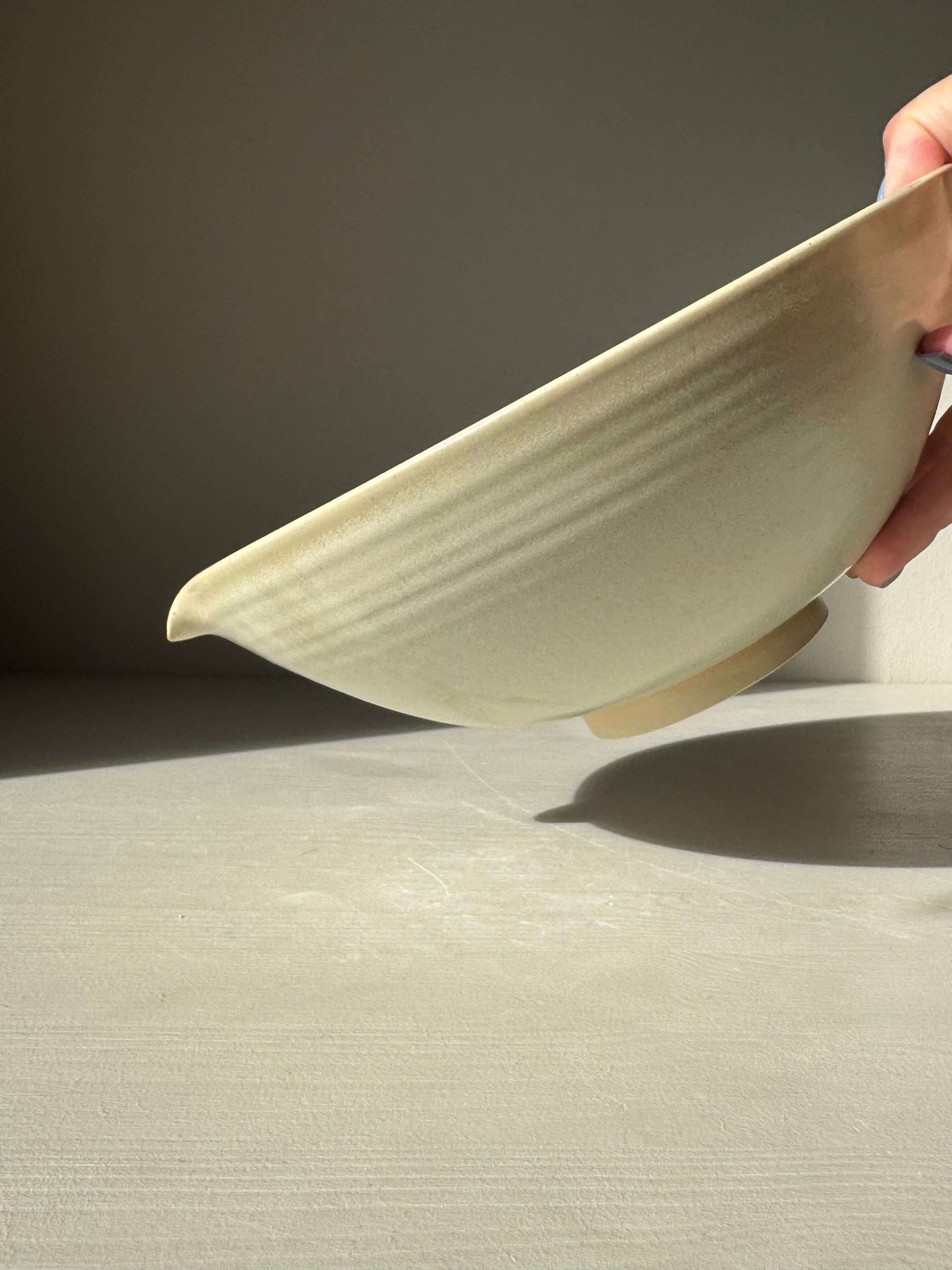 Hand holding a Pouring Bowl – Moonstone, a handmade ceramic bowl with Moonstone glaze, showcasing its carved spout and wide rim.