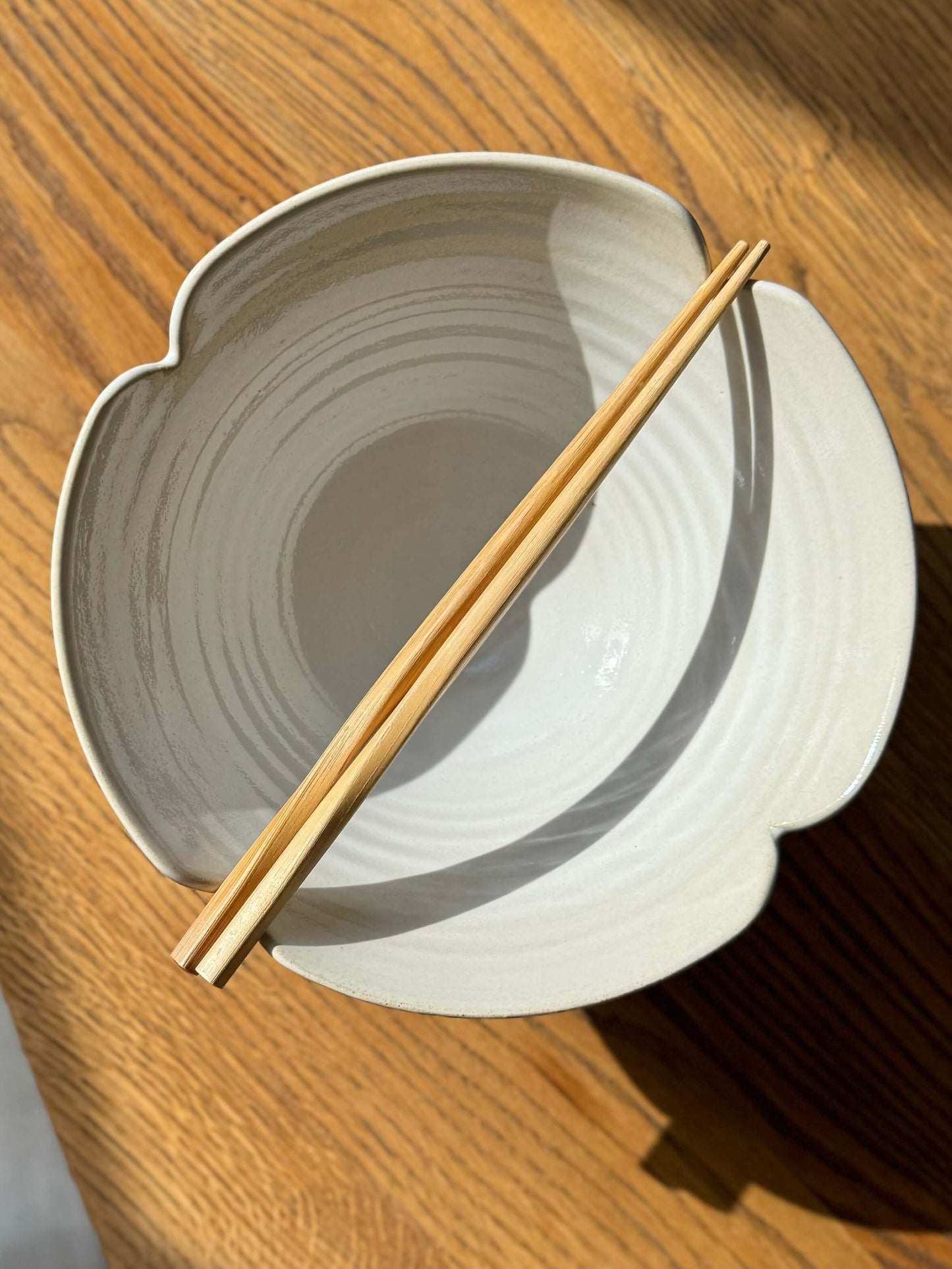 Alt Tag: Handmade white ramen bowl with scalloped flower design from Yuki Series, featuring wooden chopsticks, on wooden table.