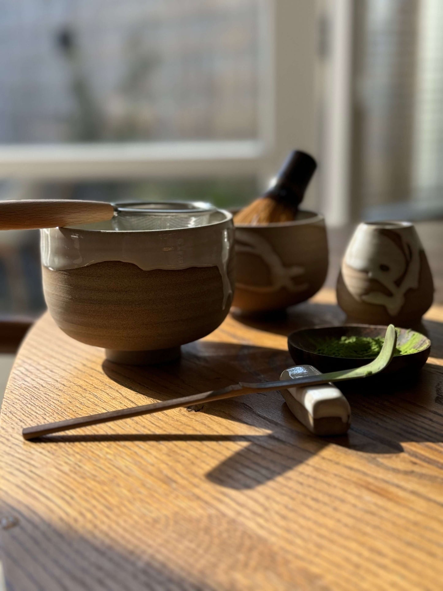 Handmade Matcha bowl from Yuki Series #01 with toffee clay and white glaze on a wooden table, tools for matcha preparation included.
