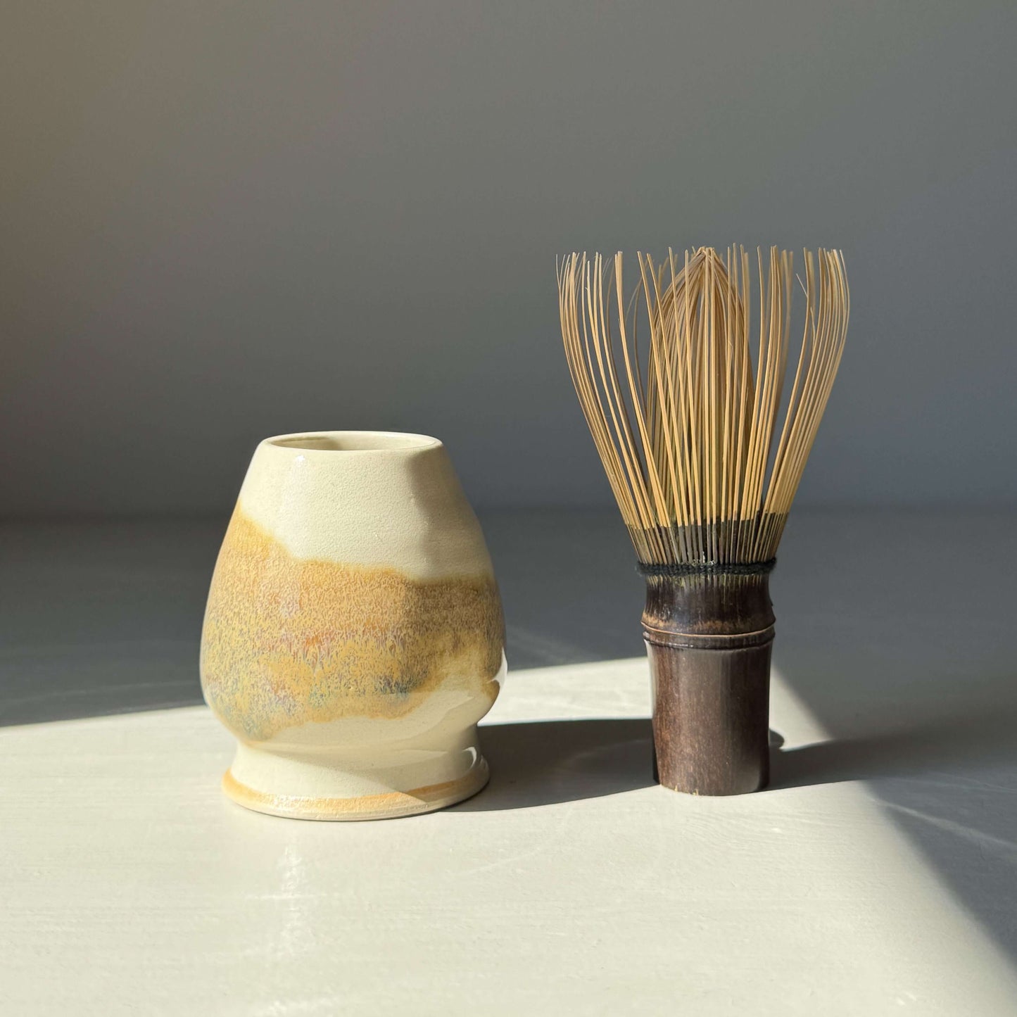 Handmade matcha whisk holder in clear glaze with bamboo whisk beside it, showcasing tenmoku splashes and earthy tones.