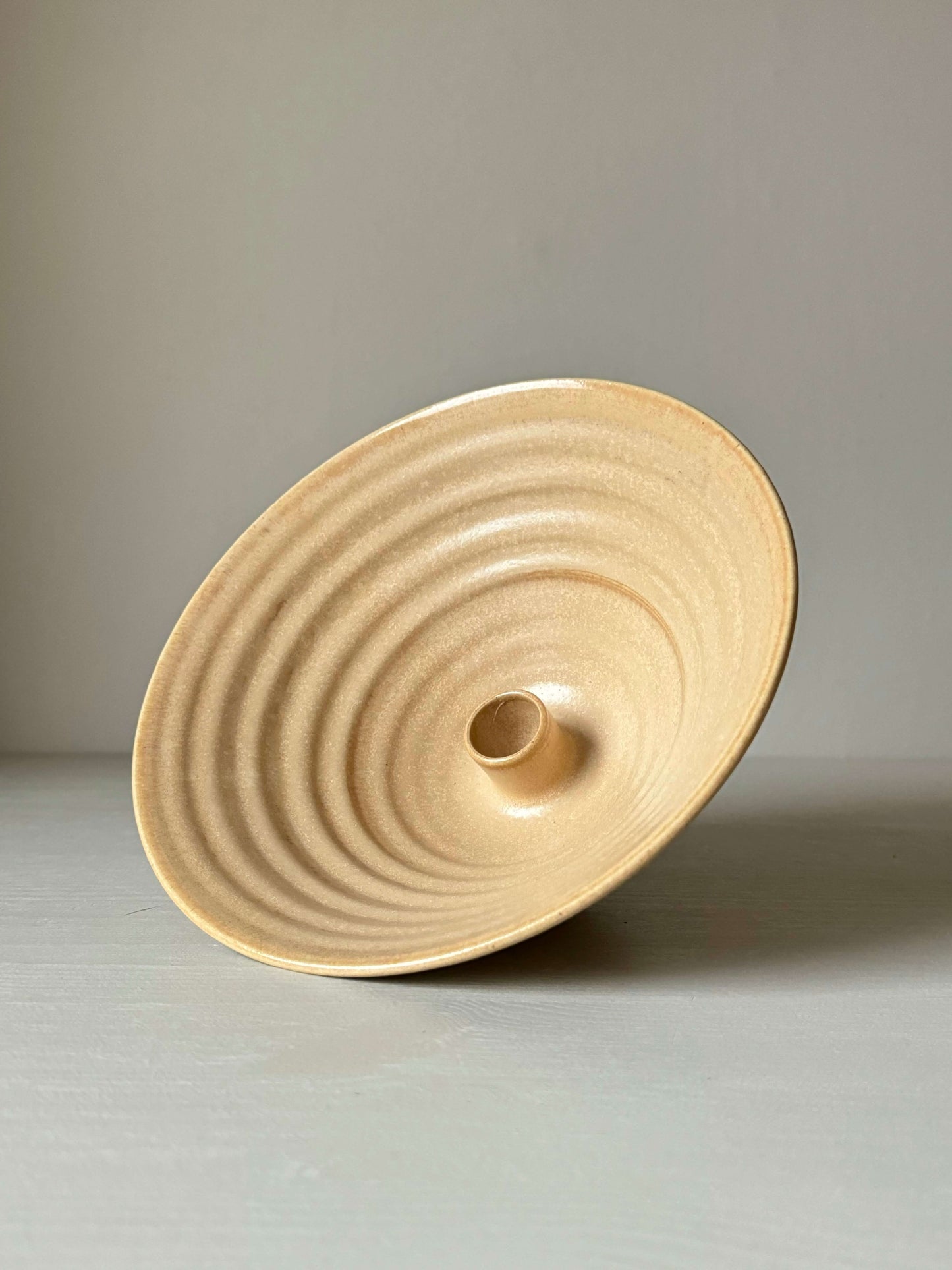 Handmade peach stoneware candlestick holder with a unique wheel-thrown design, showcasing concentric pattern, standing on a neutral background.