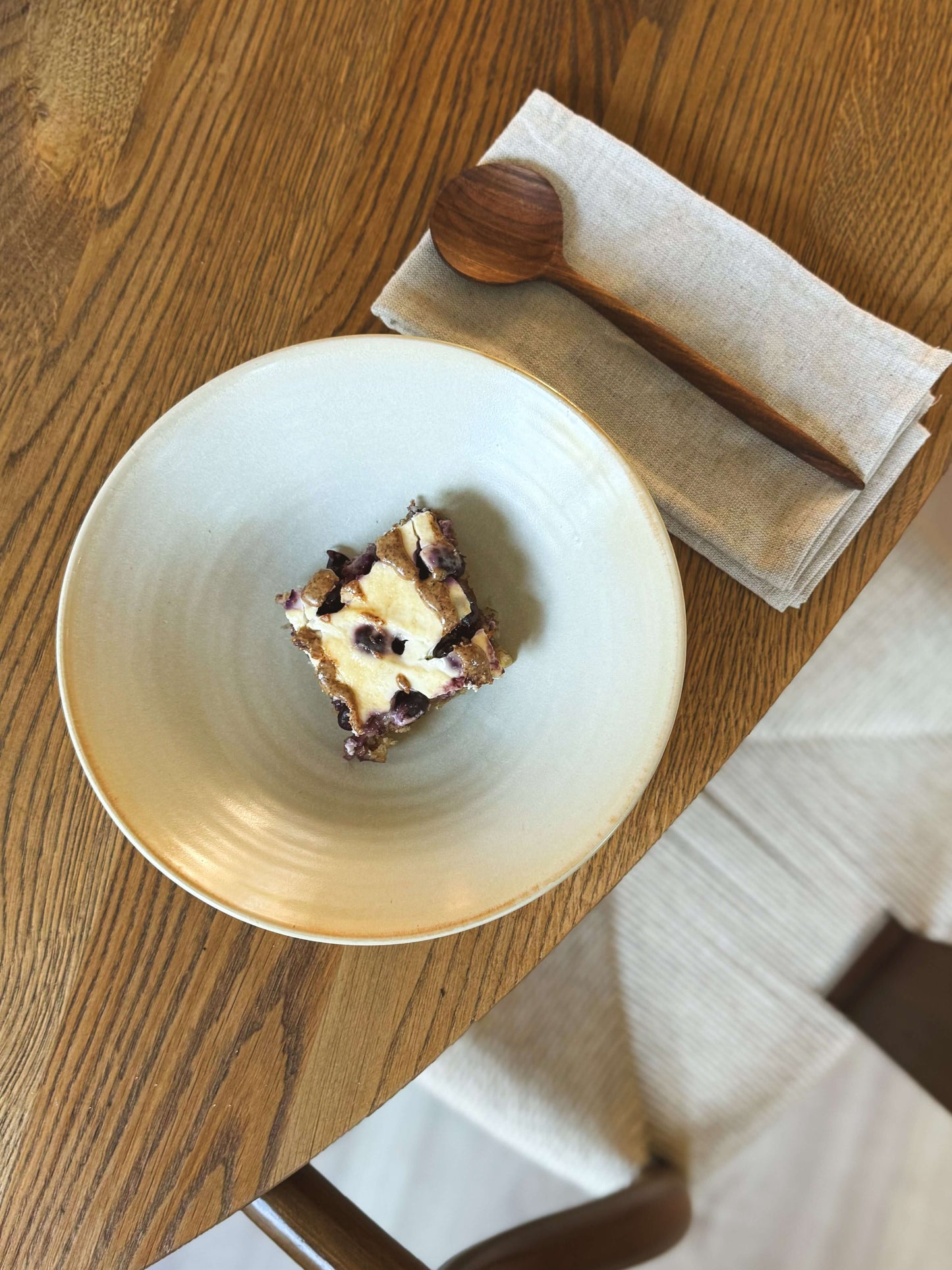 Handmade Moonstone glazed shallow dish with dessert served on a wooden table, next to a spoon and napkin.