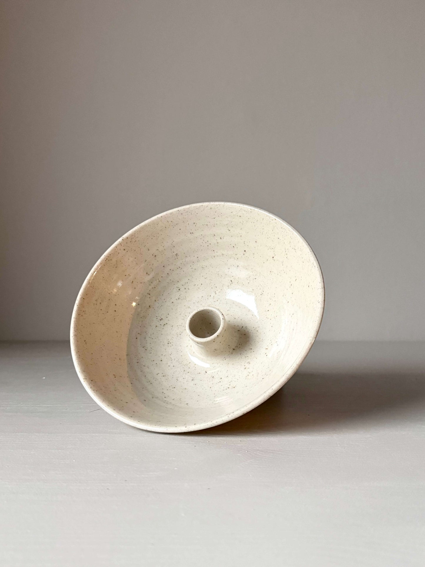 Handmade stoneware candlestick holder with clear glaze, featuring iron oxide spots, 7cm tall, 17.5cm diameter, delicate and unique design.