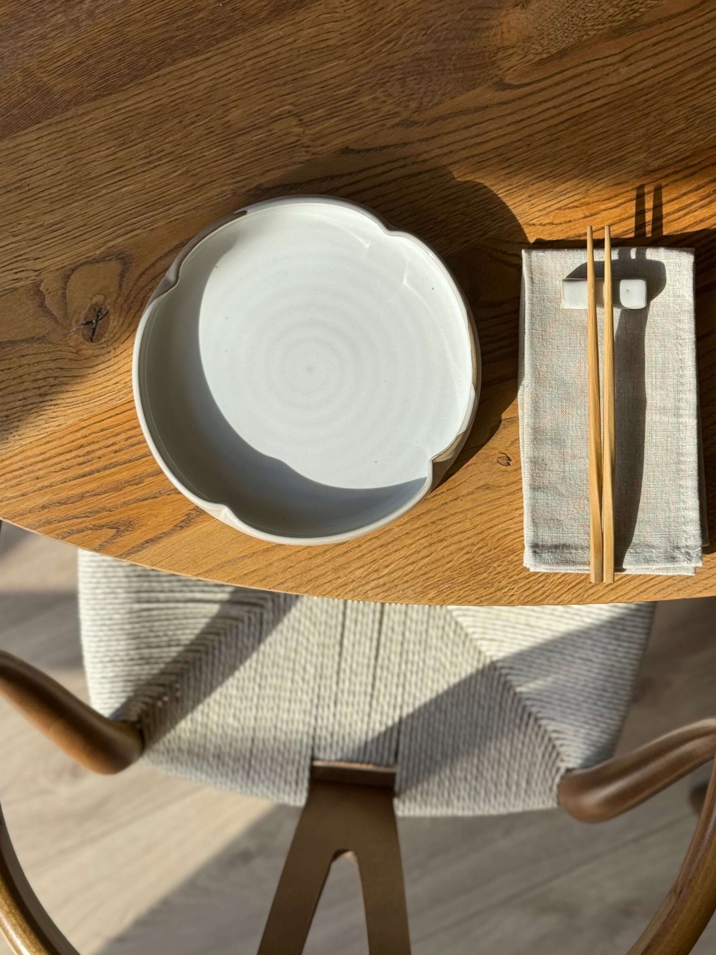Wheel-thrown large flower plate with glossy white glaze and toffee clay, placed on a wooden table with chopsticks and napkin.