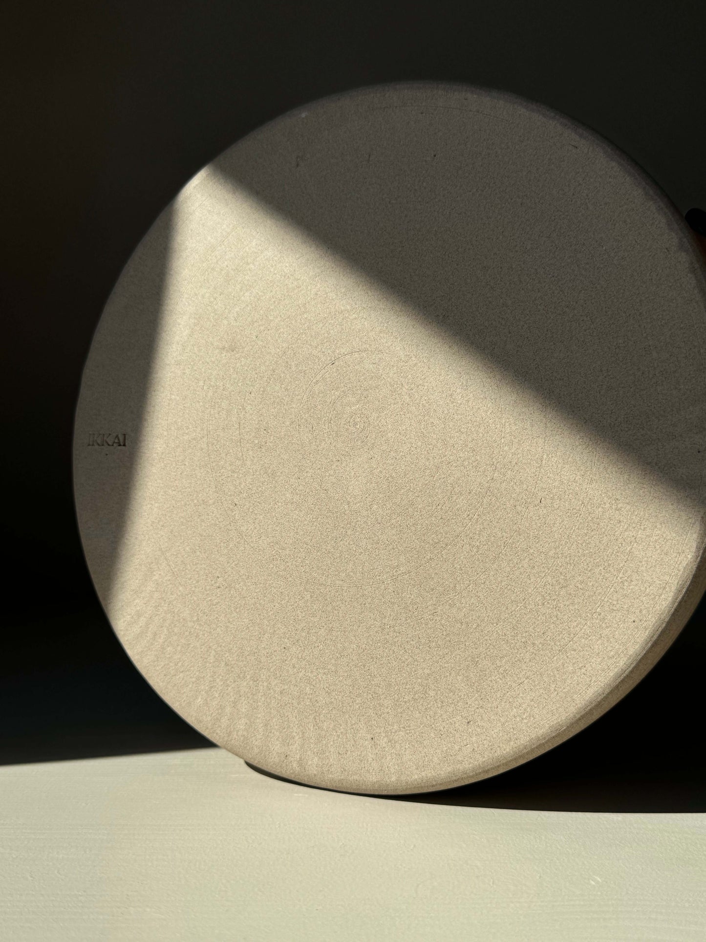 Round stoneware plate with light and shadow play on its surface, showcasing its smooth, natural texture.