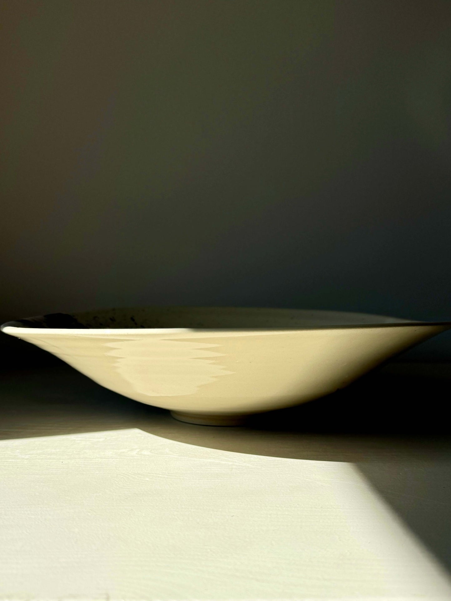 Large shallow bowl from the Gosu Series, made of durable stoneware clay, 31 cm in diameter and 7 cm in height, catching light on a table.