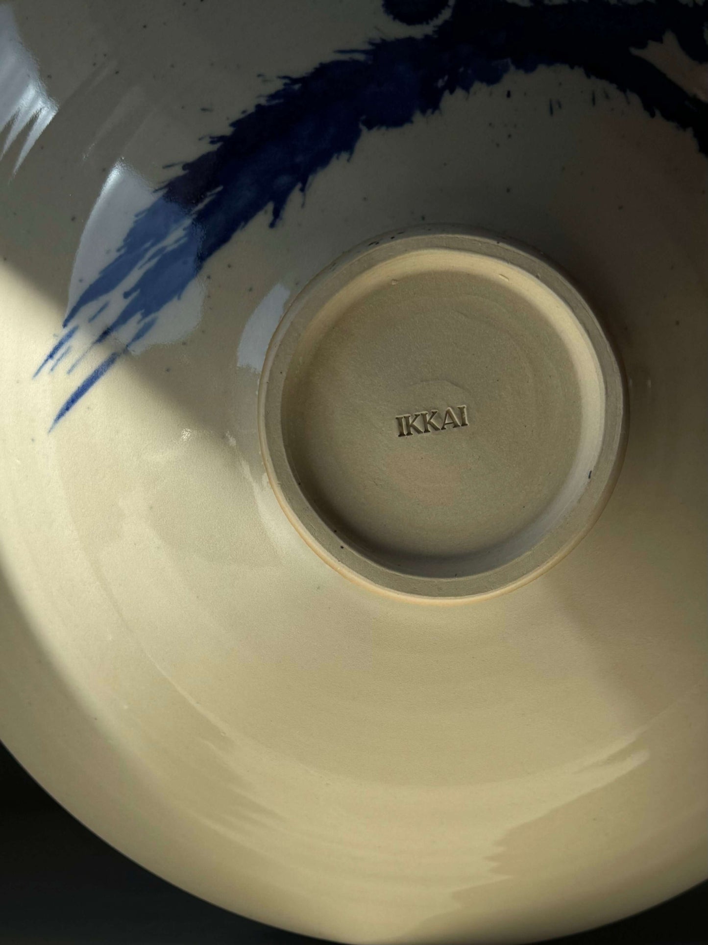 Underside of Gosu Series #04 large shallow stoneware bowl with blue brushstroke design and 'IKKAI' imprint.