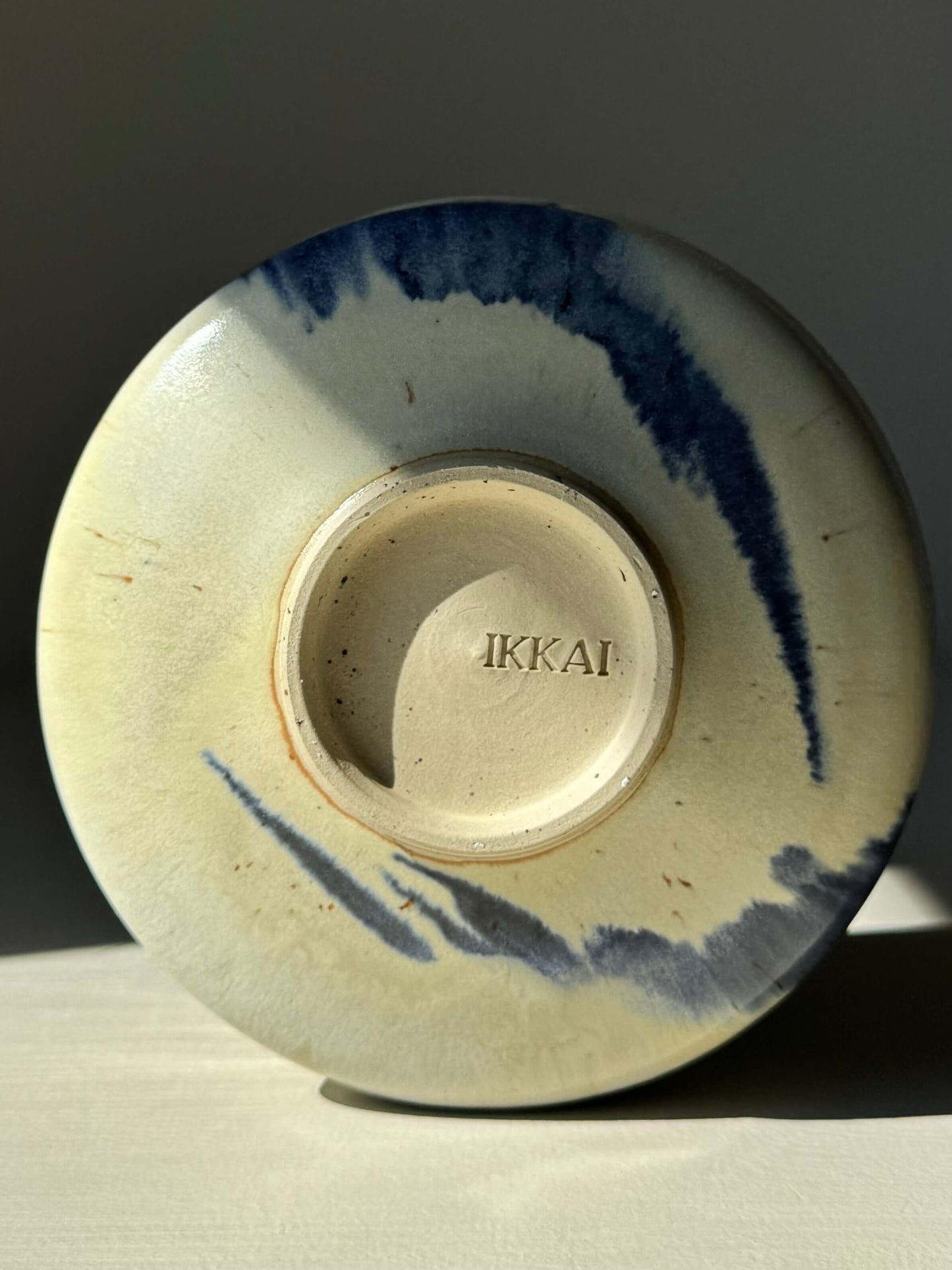 Underside of Matcha bowl with cobalt blue splashes and IKKAI branding, showcasing unique glaze design.