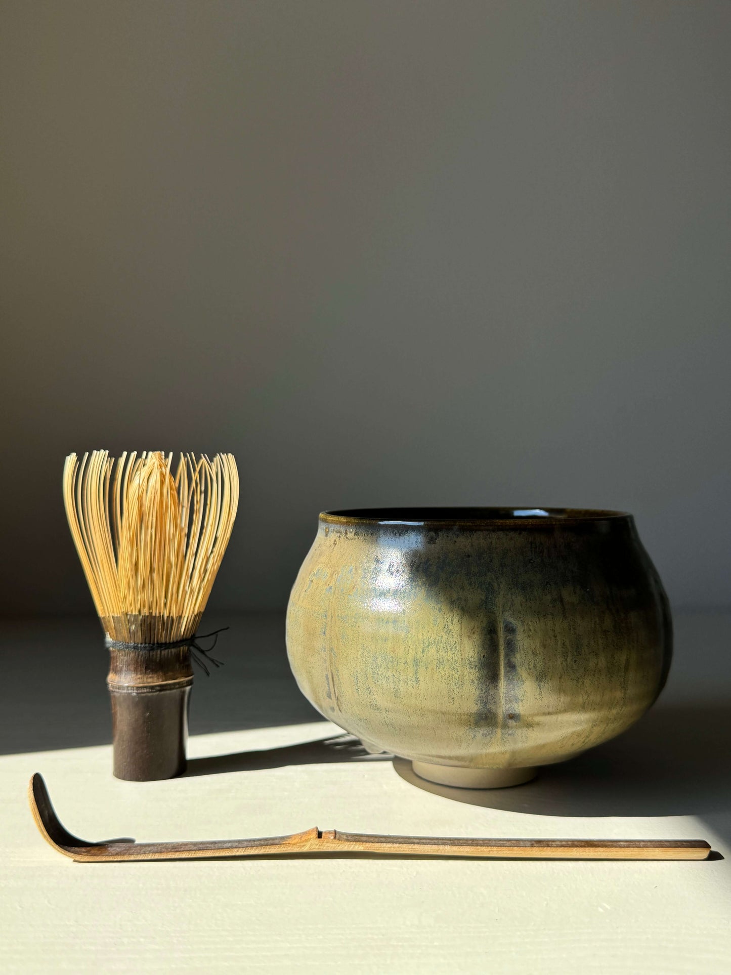Sabi Black Matcha Bowl with bamboo whisk and scoop, showcasing golden ochre and soft blue-green tones inspired by wabi-sabi.