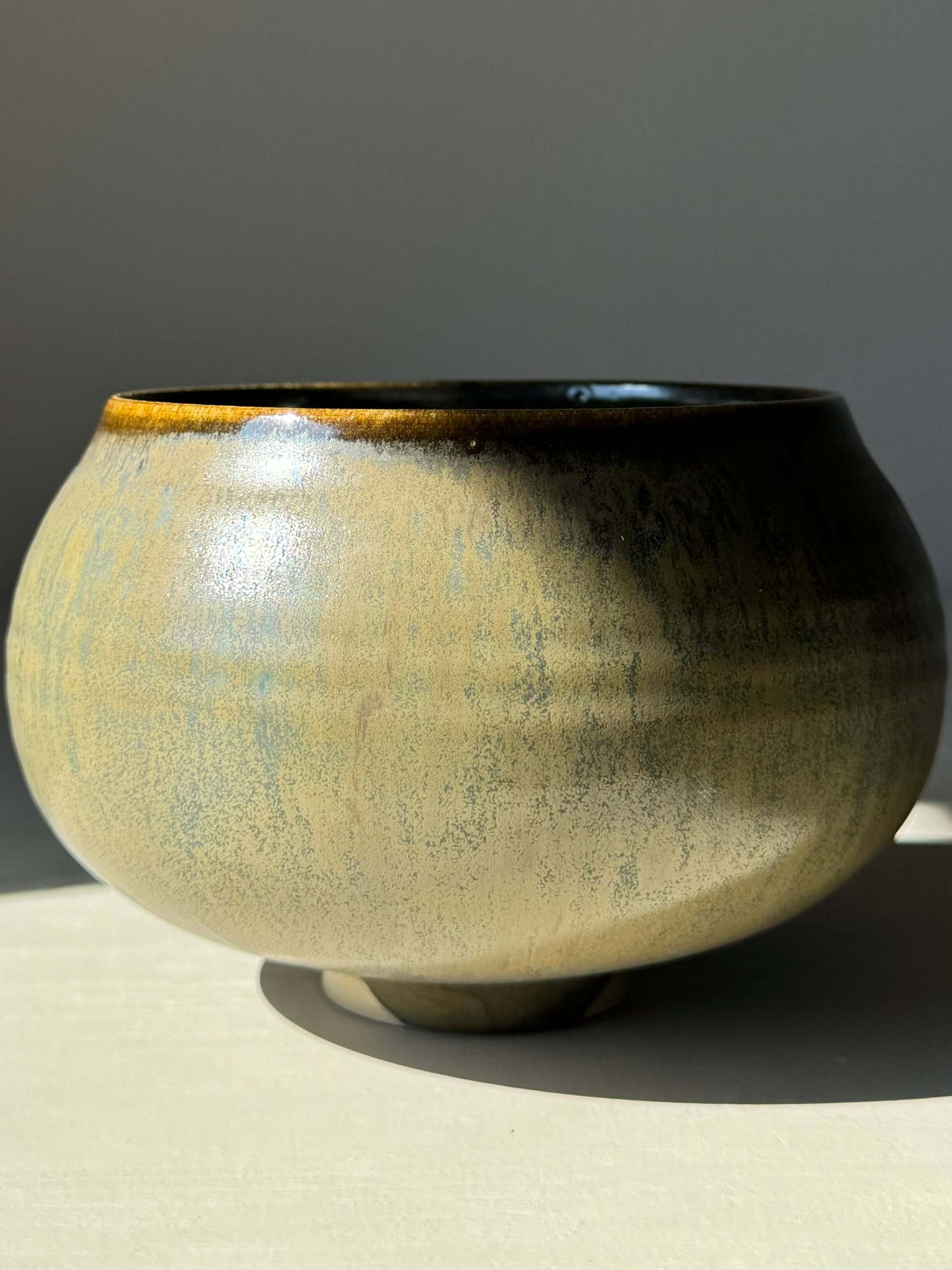 Matcha Bowl in Sabi Black with golden ochre and soft blue-green tones illuminating under light, embodying wabi-sabi elegance.