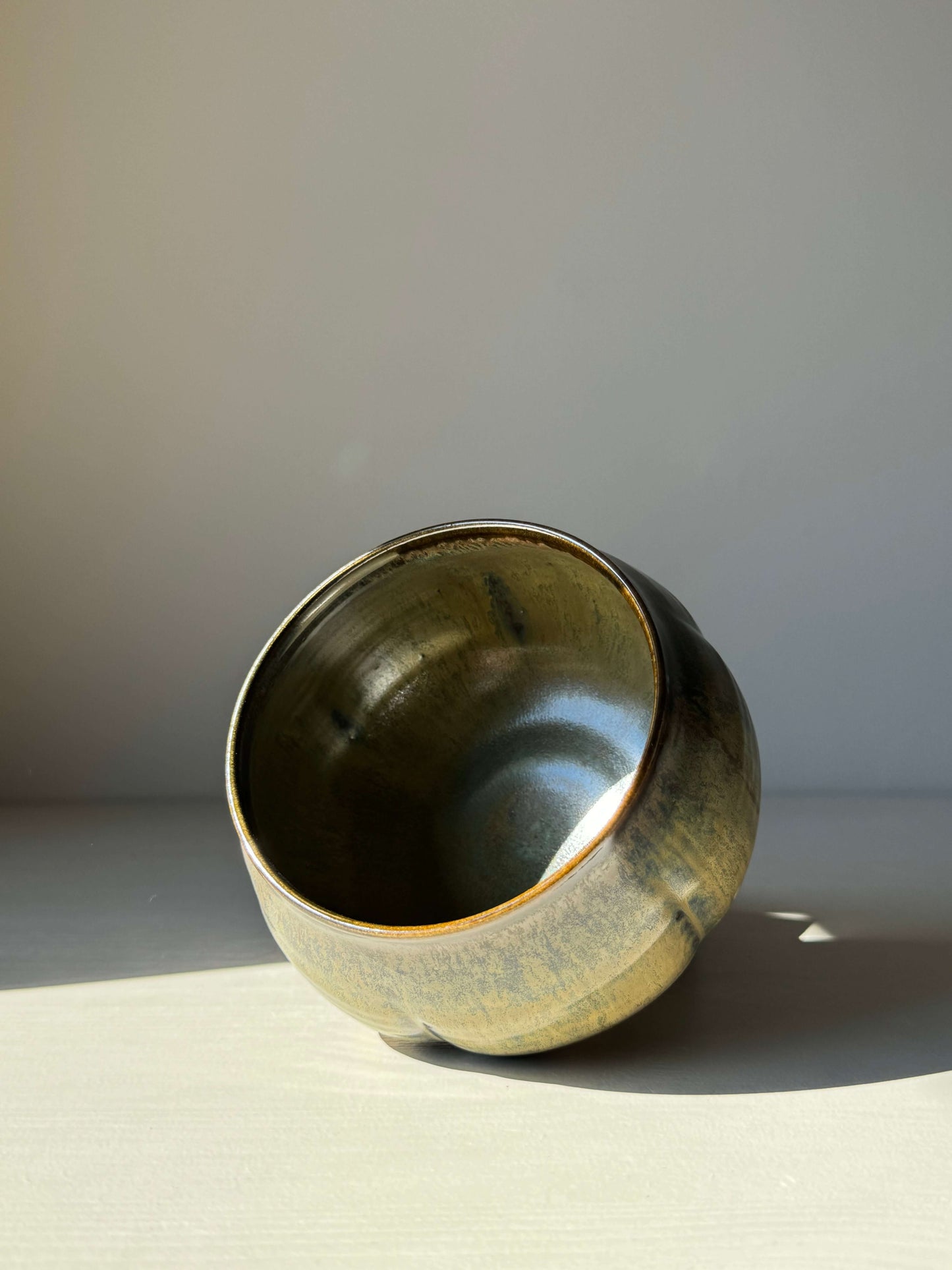 Matcha bowl with Sabi Black glaze, featuring soft black tones with golden ochre highlights and subtle blue-green hues in light.