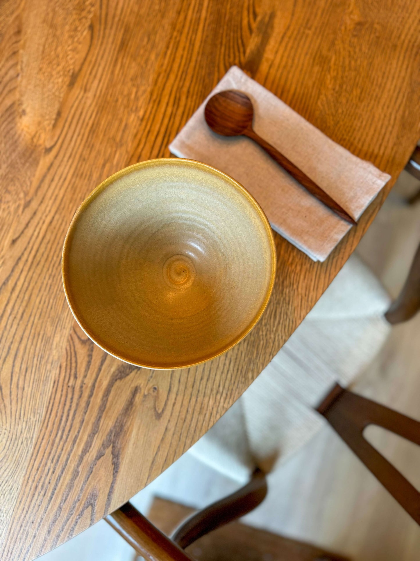 Handmade yellow glazed medium bowl on wooden table with a spoon, perfect for serving breakfast, soups, or desserts, food-safe pottery.