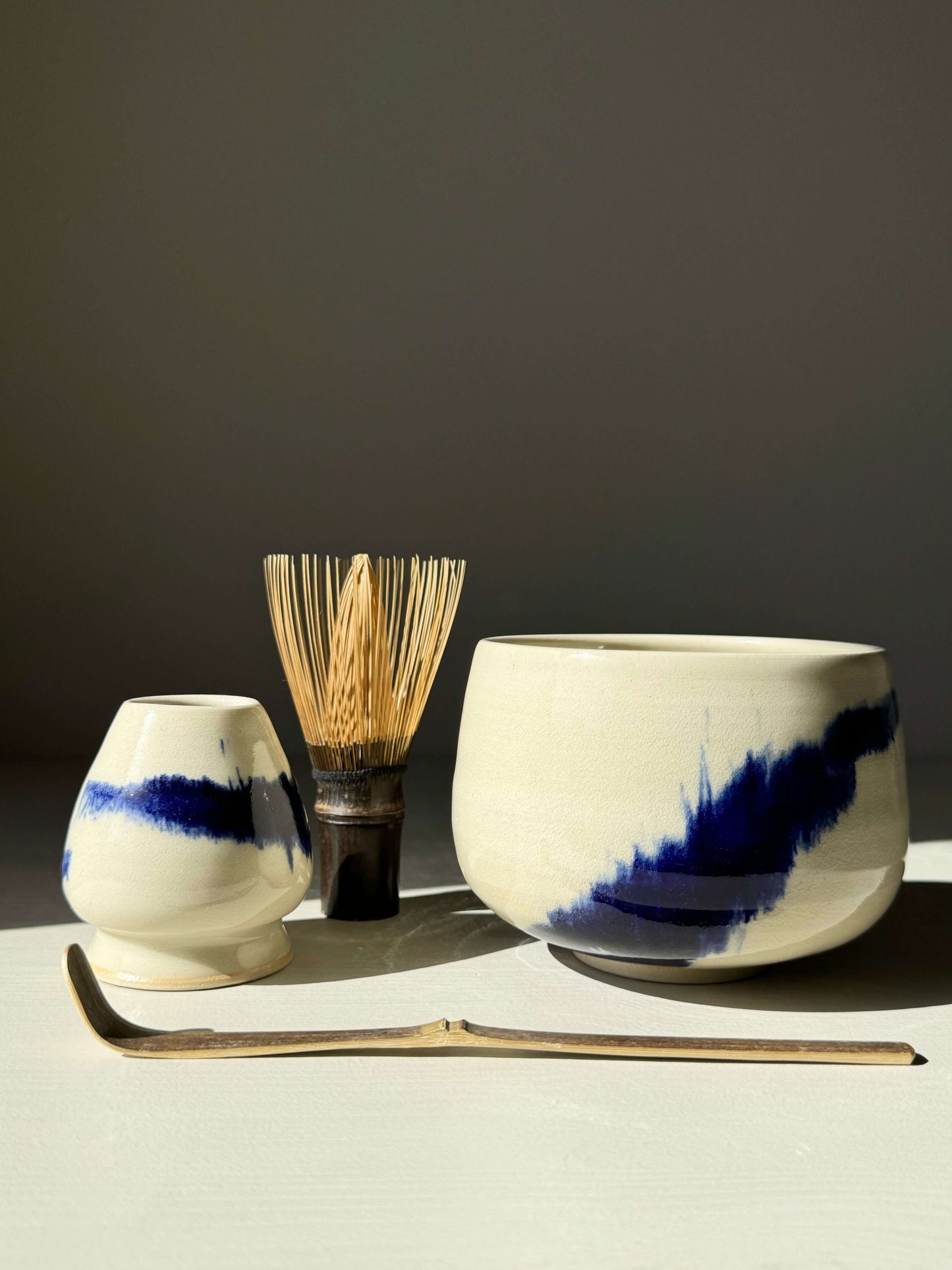 Rounded Matcha Bowl with cobalt glaze from Gosu Series, accompanied by bamboo whisk and spoon on a light background.
