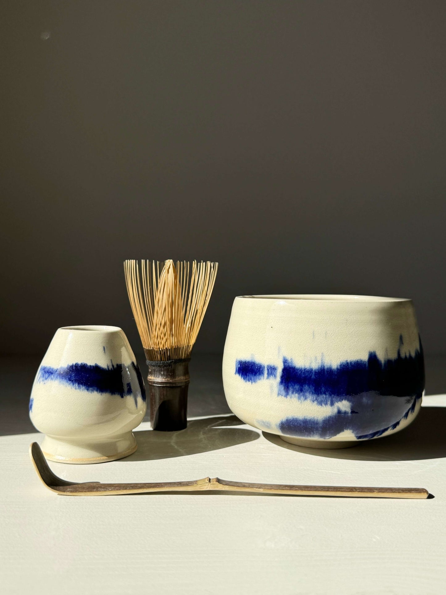 Rounded matcha bowl from Gosu Series #04 with cobalt glaze, accompanied by whisk and scoop, evoking serene natural landscapes.