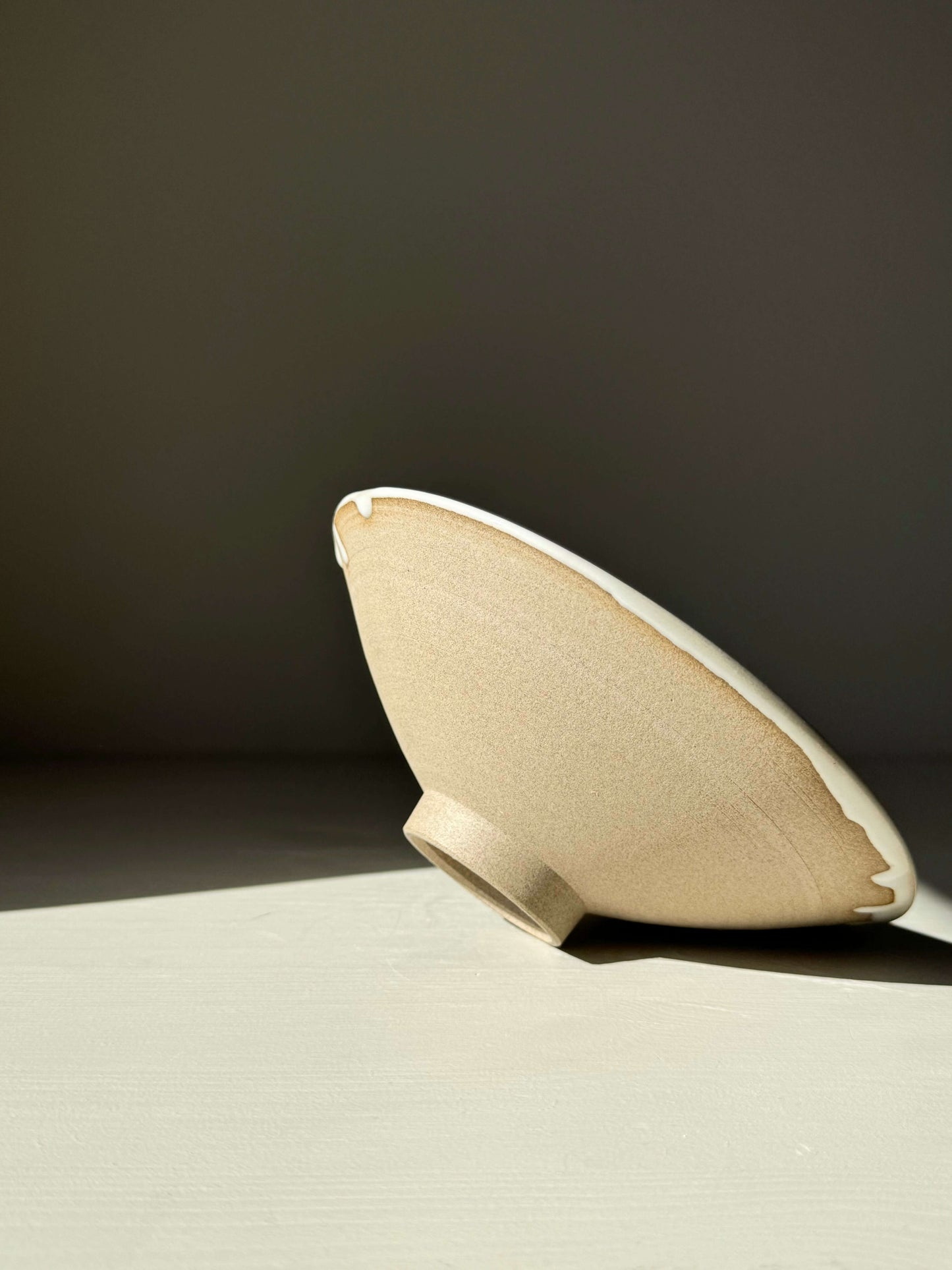 Side view of the Shallow Bowl from Yuki Series, featuring warm toffee-toned stoneware with glossy white glaze, in sunlight.