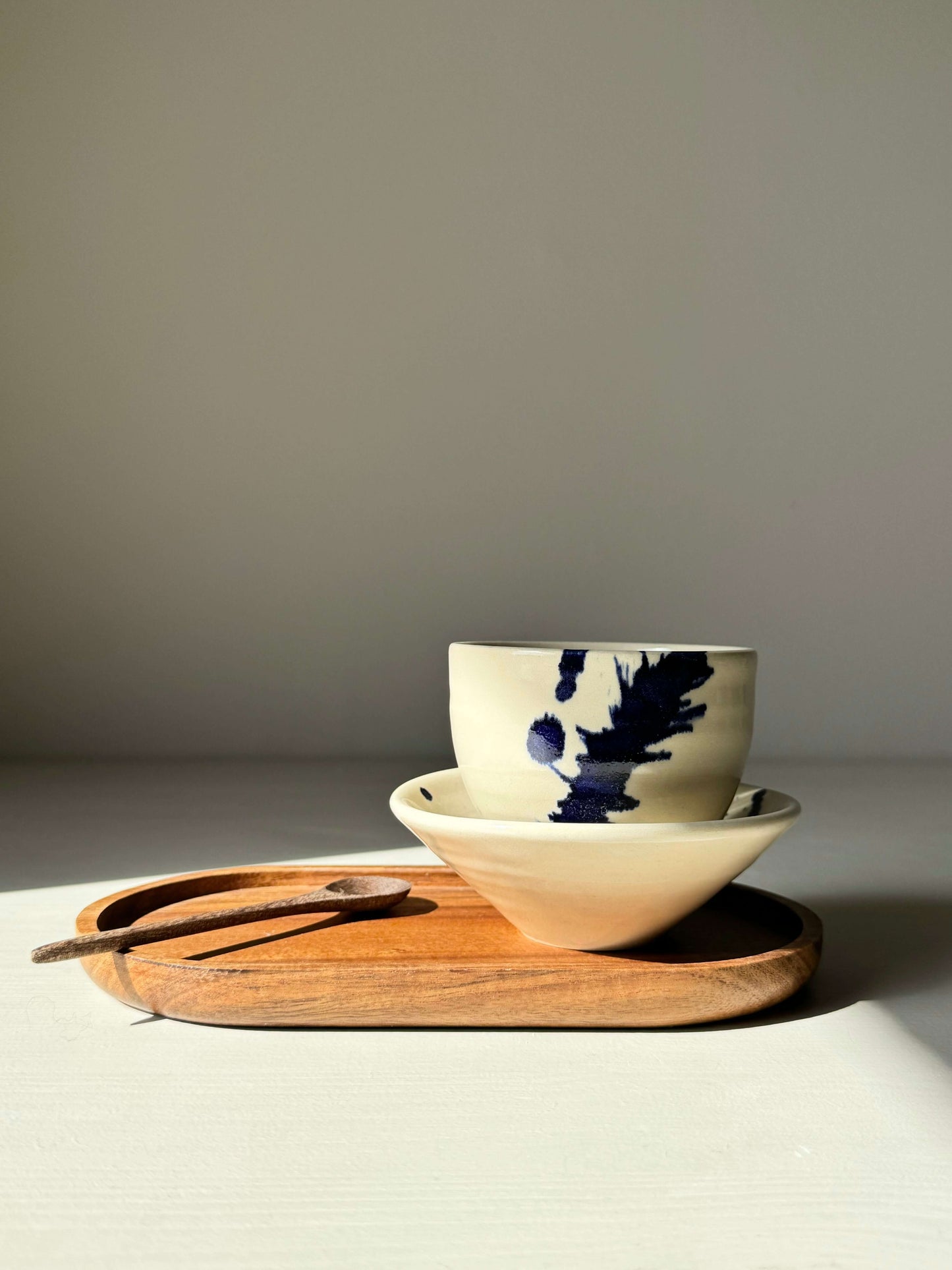Gosu Series small cup and saucer set, featuring hand-splashed cobalt details, on a wooden tray with a spoon.