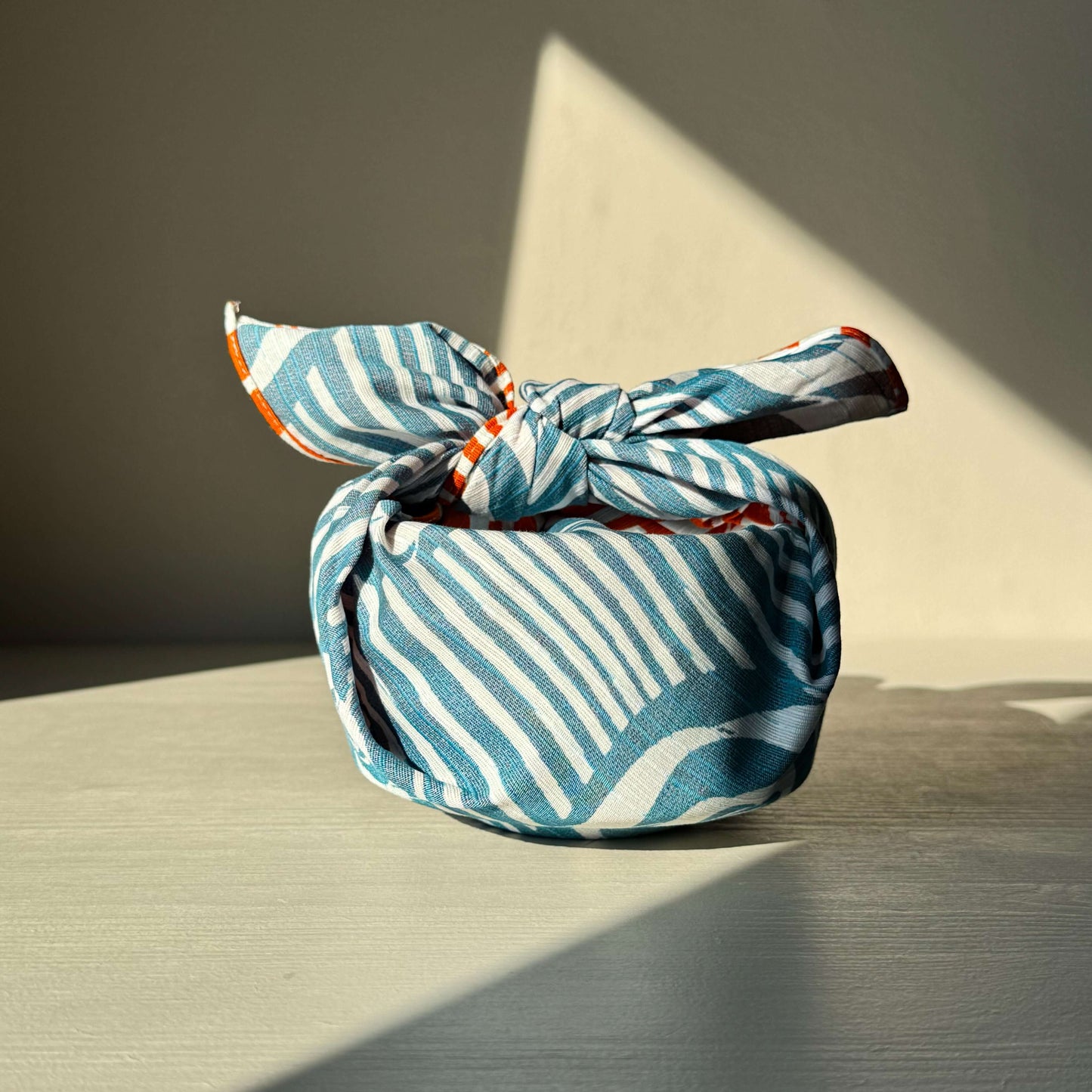 Small Furoshiki wrapped bundle featuring a Camellia Orange & Blue floral pattern, showcasing its versatility and elegance in soft lighting.