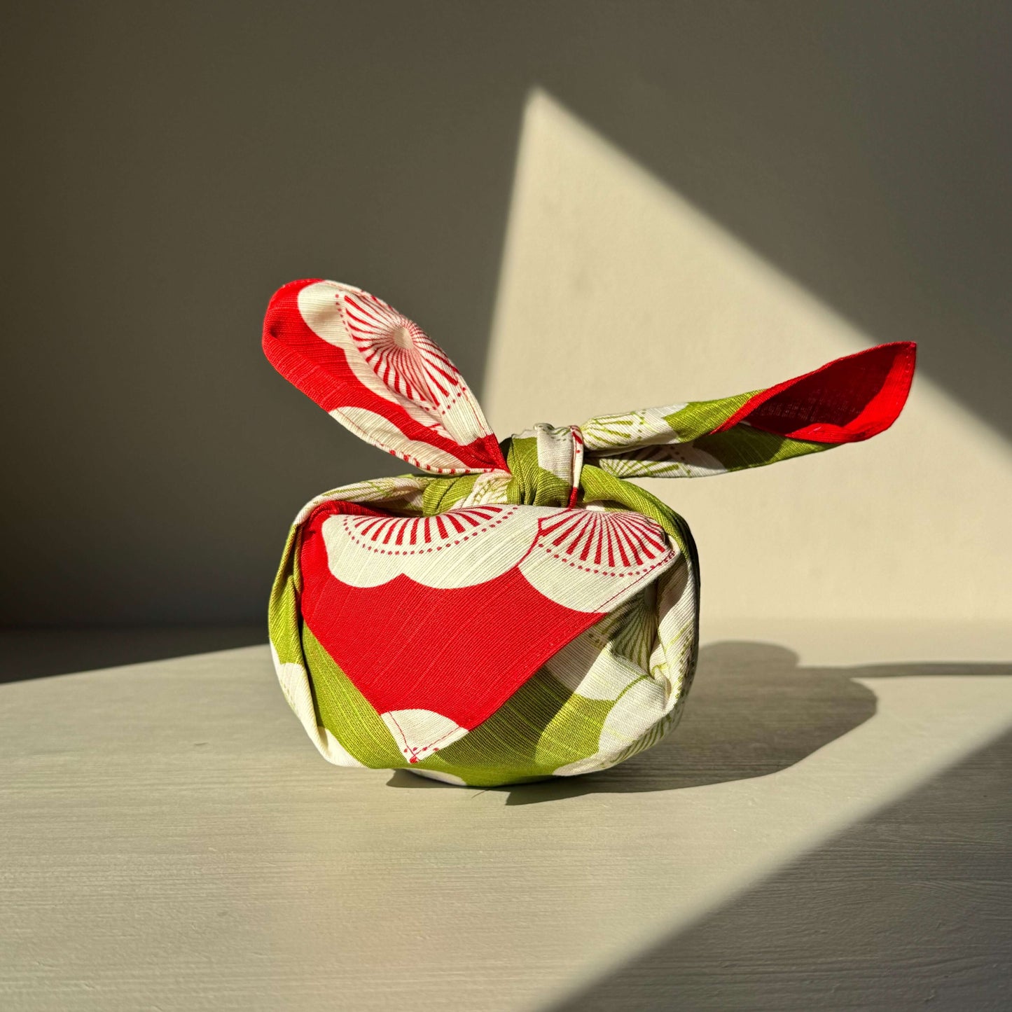 Small red and green Furoshiki wrap with plum blossom design on a light background, symbolizing Japanese culture and gift wrapping elegance.