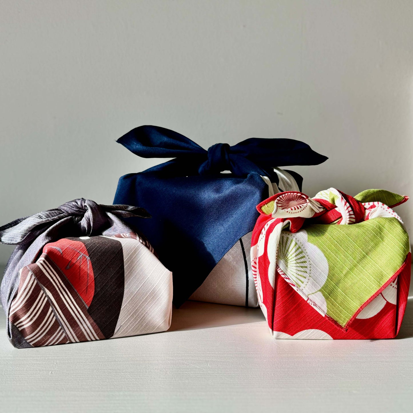 Red and green plum blossom small Furoshiki wrapping cloth alongside two others, symbolizing happiness and elegance in Japanese culture.