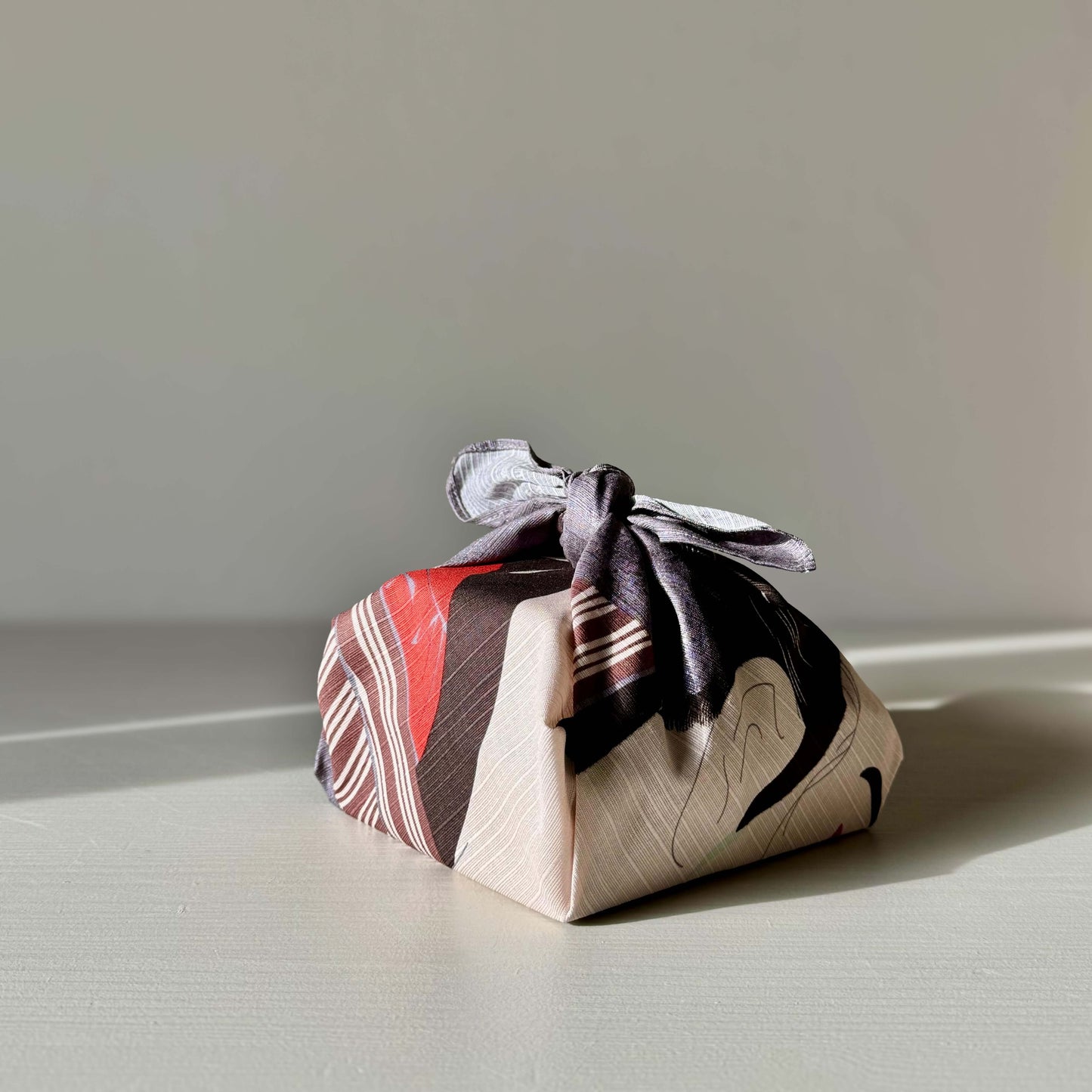 Small Furoshiki - Sharaku Gray wrapping a gift, showcasing reusable cotton fabric with handmade ceramic accents.