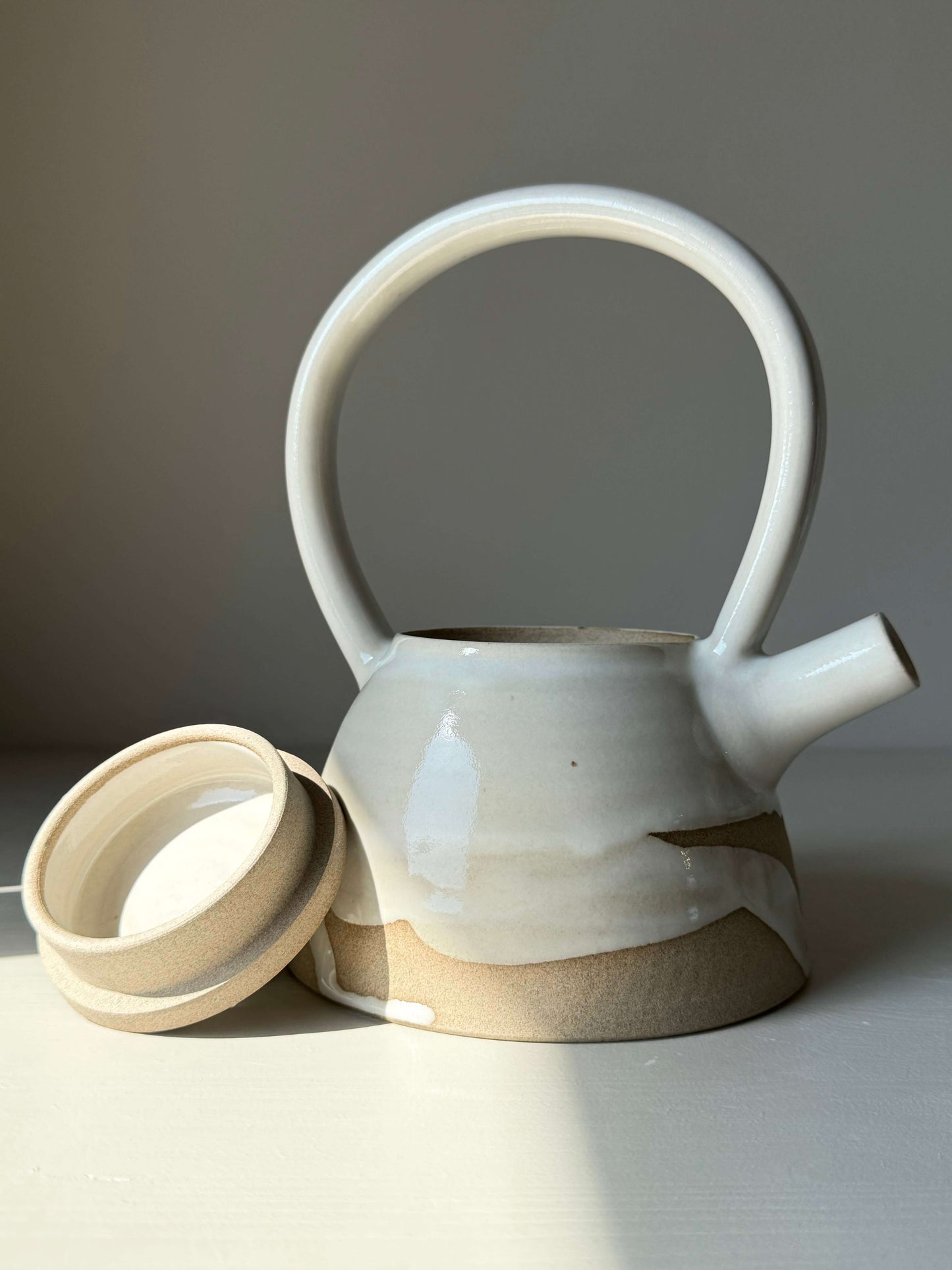 Yuki Series #03 teapot with tall, looped handle and soft curves, featuring white glaze and unglazed clay base.