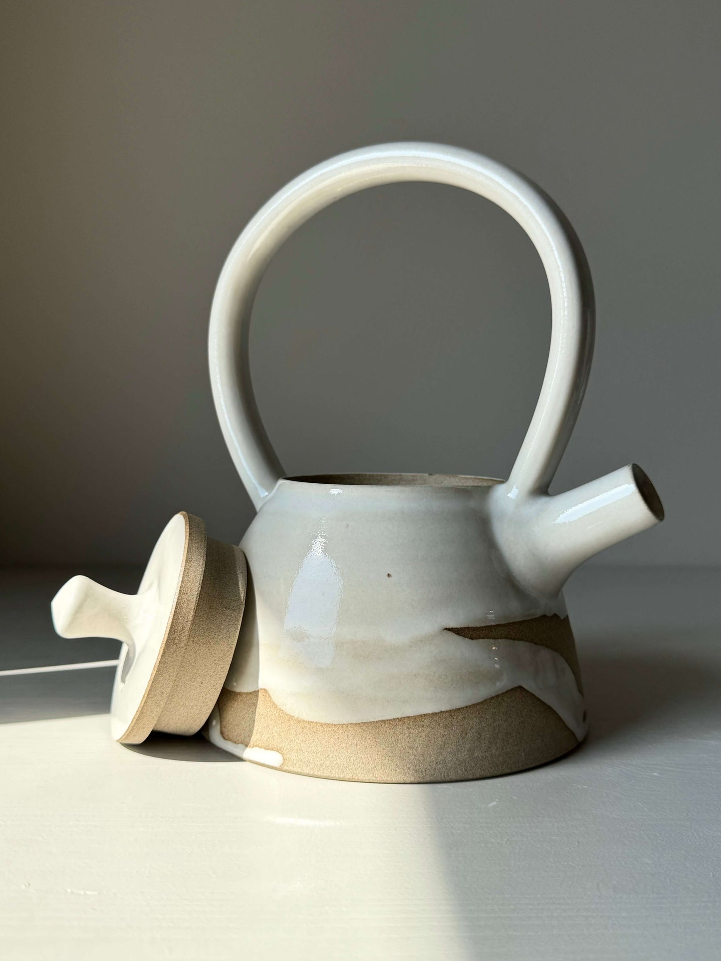 Yuki Series #03 teapot with tall looped handle, white glaze, and unglazed clay base, blending sculptural design with natural texture.