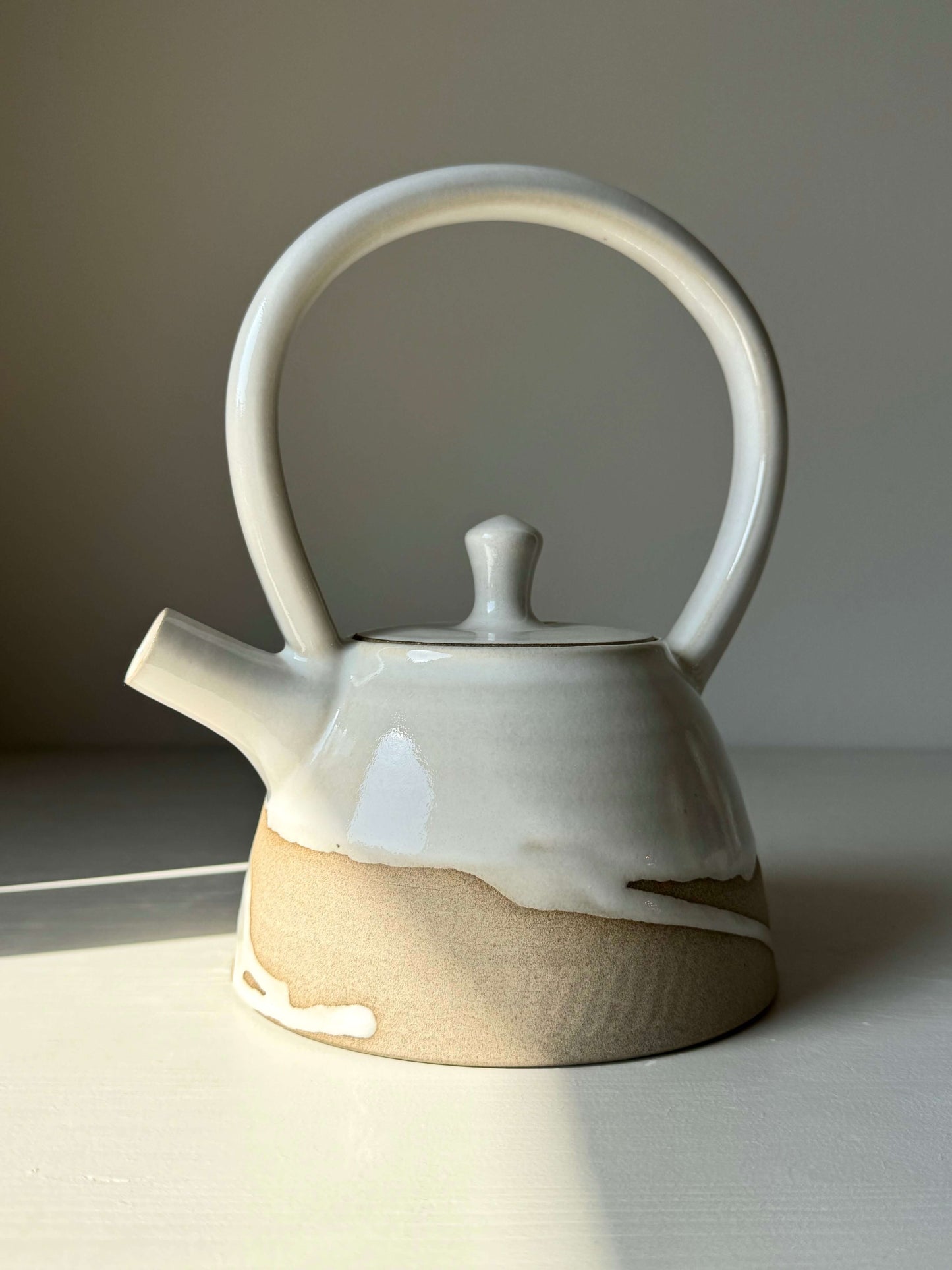 Elegant Yuki Series #03 teapot with tall looped handle, soft curves, and white glaze contrasting with unglazed warm clay base.