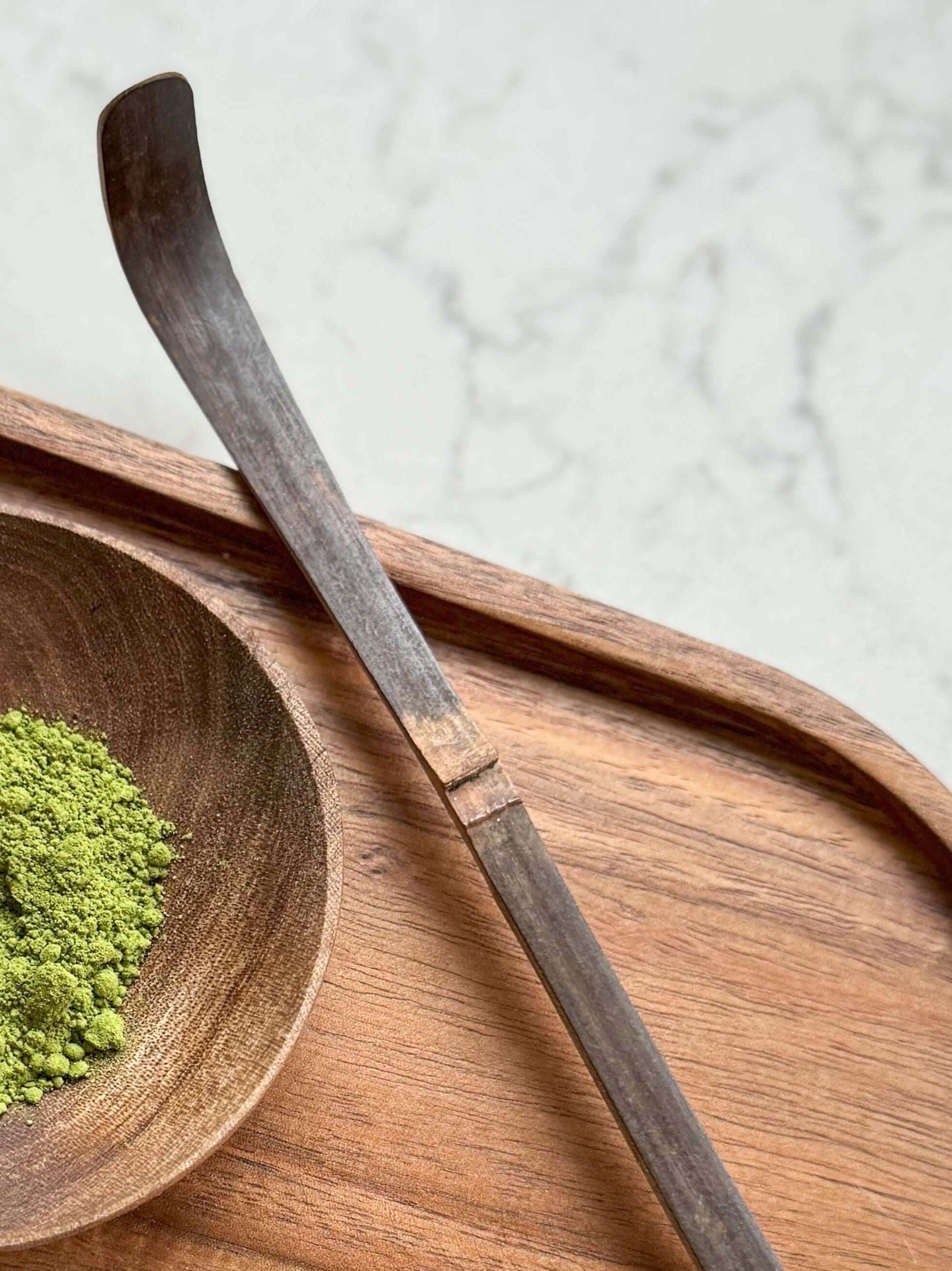 Traditional Matcha Spoon (Chashaku) – Dark Brown handmade ceramic tool on wooden tray next to matcha powder, made from dark bamboo.