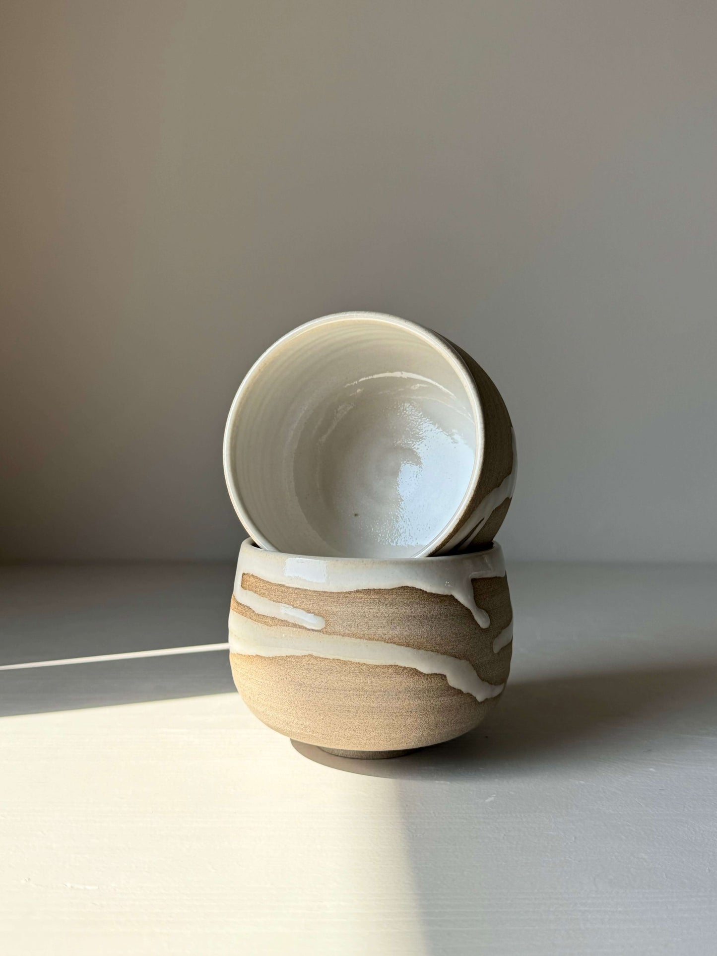 Two Yuki Series coffee cups with toffee clay and white glaze, showcasing unique flowing patterns in natural light.