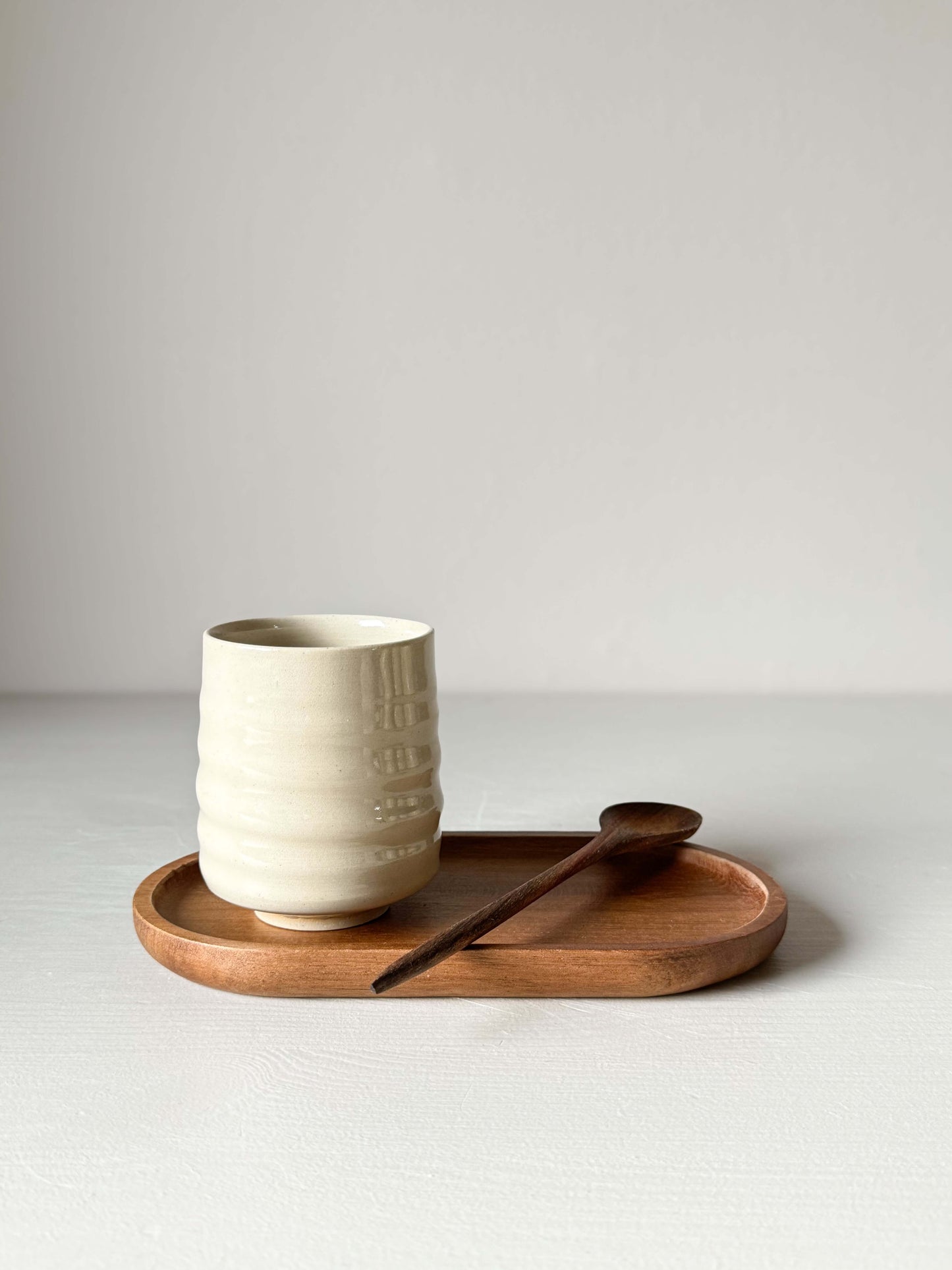 Yunomi Cup with clear glaze on a wooden tray, featuring a compact design. Wheel-thrown stoneware with a small wooden spoon beside it.