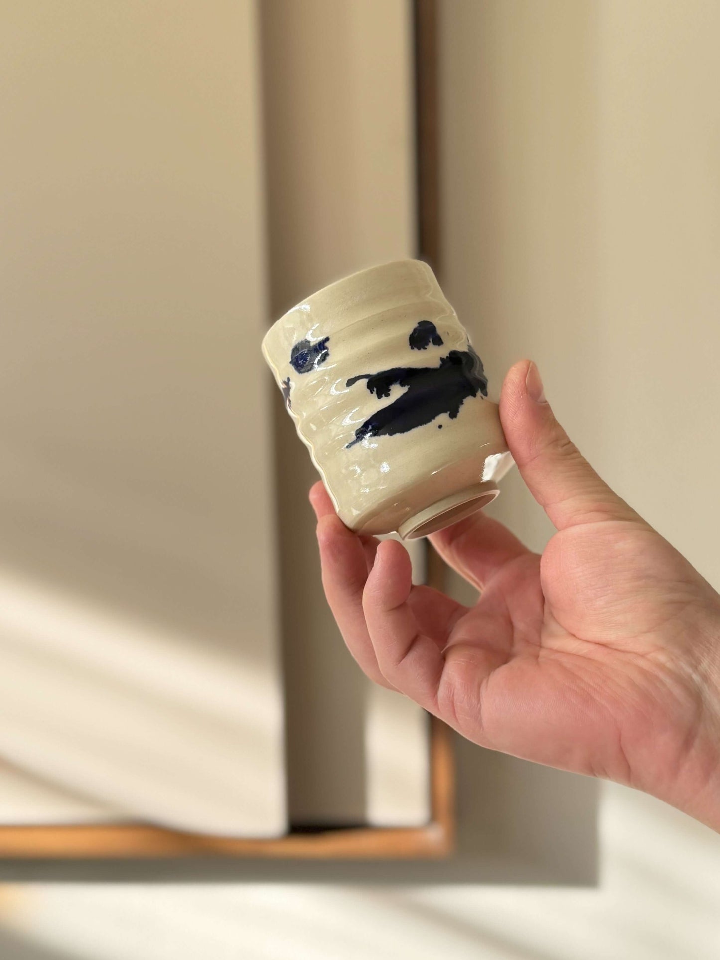 Hand holding a Yunomi Cups - Gosu Series handmade ceramic, showcasing cobalt blue splashes on a clear glazed surface.