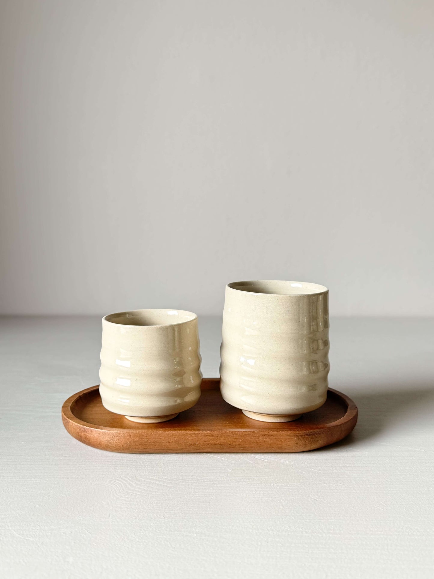 Wheel-thrown Yunomi cups with clear glaze on wooden tray, 8.5cm and 6.5cm sizes, high-fired stoneware, 225ml capacity.