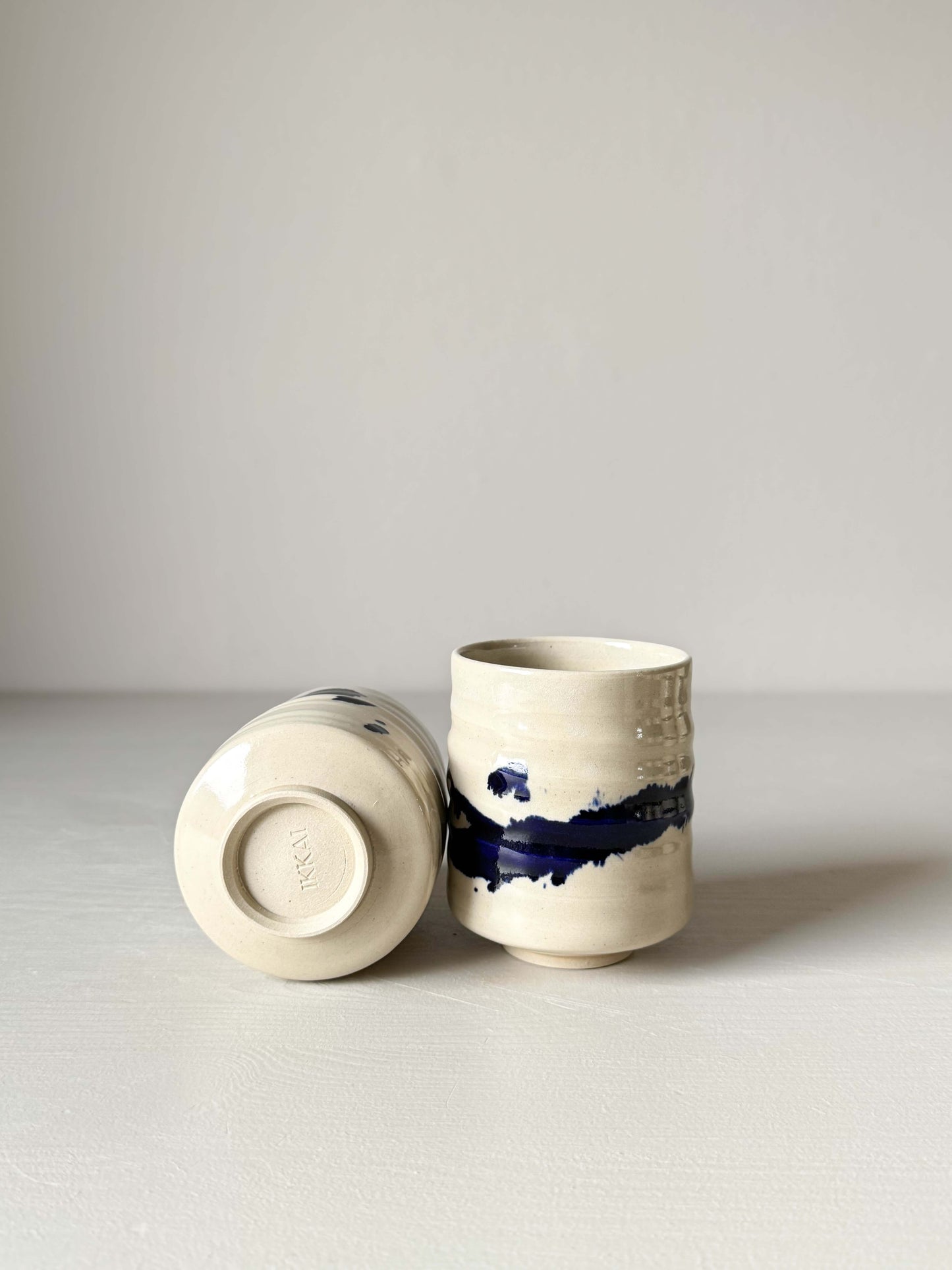 Handmade ceramic Yunomi Cups - Gosu Series with cobalt blue splashes on a gray background.