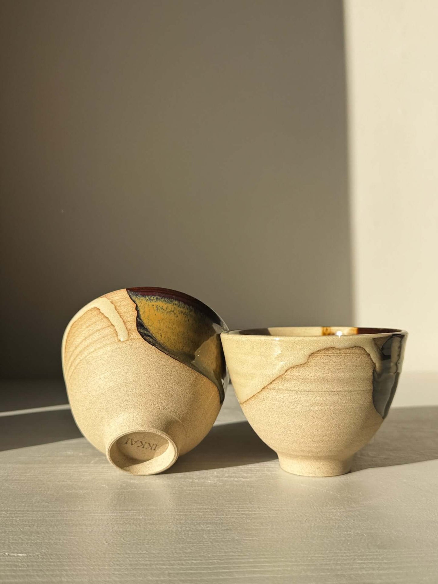 Yunomi Cups - Inyo #01 with unique glazes in gold, brown, and blue, showcasing the classic rounded shape on a pale background.